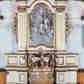 Zdjęcie nr 1: Oprawa chrzcielnicy architektoniczna jednoosiowa, jednokondygnacyjna ze zwieńczeniem, ustawiona na czterostrefowym cokole wyłamanym na osi podpór, w środkowej przestrzeni chrzcielnica; w drugiej od dołu strefie silnie wysunięte do przodu wsporniki podtrzymywane przez konsole dekorowane liśćmi akantu; trzy strefy cokołu zdobione płycinami. Kondygnacja węższa od podstawy, ujęta parą pilastrów o kanelowanych trzonach i kapitelach kompozytowych wspierających pełne belkowanie wyłamane na ich osi, nad polem środkowym przyjmujące kształt łuku odcinkowego. W polu środkowym płycina ujęta profilowaną ramą w formie stojącego prostokąta zamkniętego łukiem półkolistym nadwieszonym z uskokiem z płaskorzeźbioną sceną Chrztu Chrystusa z sygnaturą „1885 / P(AWEŁ) TURBAS”. Kondygnacja ujęta uszami utworzonymi z wici roślinnej z kwiatami. Zwieńczenie w formie stojącego prostokąta o wklęsłych bokach przechodzących w duże woluty spływające na belkowanie, zamknięte dwoma falistymi fragmentami gzymsu przechodzącymi w przeciwstawnie zwrócone woluty; całość zakończona szczytem utworzonym z muszli flankowanej kwiatowymi festonami. W polu płycina w formie zbliżonej do zwieńczenia z płaskorzeźbioną półpostacią aniołka na obłoku, z rękoma rozłożonymi na boki. Struktura polichromowana w kolorze białym ze złoconymi profilami i ornamentyką oraz srebrzoną płaskorzeźbą. 