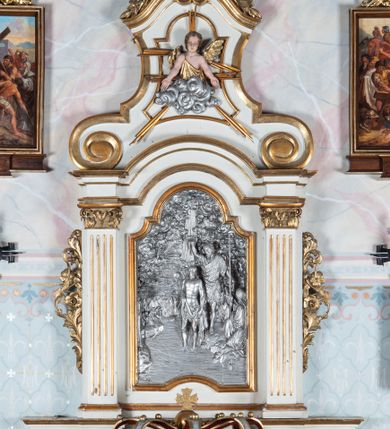 Zdjęcie nr 1: Oprawa chrzcielnicy architektoniczna jednoosiowa, jednokondygnacyjna ze zwieńczeniem, ustawiona na czterostrefowym cokole wyłamanym na osi podpór, w środkowej przestrzeni chrzcielnica; w drugiej od dołu strefie silnie wysunięte do przodu wsporniki podtrzymywane przez konsole dekorowane liśćmi akantu; trzy strefy cokołu zdobione płycinami. Kondygnacja węższa od podstawy, ujęta parą pilastrów o kanelowanych trzonach i kapitelach kompozytowych wspierających pełne belkowanie wyłamane na ich osi, nad polem środkowym przyjmujące kształt łuku odcinkowego. W polu środkowym płycina ujęta profilowaną ramą w formie stojącego prostokąta zamkniętego łukiem półkolistym nadwieszonym z uskokiem z płaskorzeźbioną sceną Chrztu Chrystusa z sygnaturą „1885 / P(AWEŁ) TURBAS”. Kondygnacja ujęta uszami utworzonymi z wici roślinnej z kwiatami. Zwieńczenie w formie stojącego prostokąta o wklęsłych bokach przechodzących w duże woluty spływające na belkowanie, zamknięte dwoma falistymi fragmentami gzymsu przechodzącymi w przeciwstawnie zwrócone woluty; całość zakończona szczytem utworzonym z muszli flankowanej kwiatowymi festonami. W polu płycina w formie zbliżonej do zwieńczenia z płaskorzeźbioną półpostacią aniołka na obłoku, z rękoma rozłożonymi na boki. Struktura polichromowana w kolorze białym ze złoconymi profilami i ornamentyką oraz srebrzoną płaskorzeźbą. 