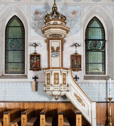 Zdjęcie nr 1: Ambona wisząca, przyścienna, z wejściem od prawej strony. Kosz na planie ośmioboku, na niskim cokole, od dołu ujęty ośmiobocznym podwieszeniem. Ścianki kosza zdobione prostokątnymi płycinami wypełnionymi stylizowaną wicią liści akantu z czteropłatkowym kwiatkiem pośrodku. Parapet w formie prostego belkowania, którego imposty wsparte są małymi hermami – główkami połączonymi z dekoracją naśladującą ornament małżowinowo-chrząstkowy. Zaplecek w kształcie stojącego prostokąta w profilowanej i złoconej ramie, w górnej partii ujęty po bokach wicią akantu ze stylizowanymi podwieszonymi kampanulami; w polu umieszczone tablice dekalogu na obłokach. Baldachim  na planie ośmioboku, z wydatnym, profilowanym gzymsem, zwieńczony kabłąkami spiętymi i podtrzymującymi krzyżyk łaciński zatknięty na kuli. Na podniebieniu baldachimu, w ośmiobocznej płycinie rzeźbiona gołębica Ducha Świętego na tle promienistej glorii złożonej z wiązek promieni o nierównej długości. Balustrada schodów zdobiona wydłużonym, stylizowanym ornamentem małżowinowo-chrząstkowym umieszczonym w płytkiej, romboidalnej płycinie. Struktura polichromowana w kolorze beżowym, profile i ornamenty złocone oraz posrebrzone.