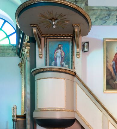 Zdjęcie nr 1: Ambona wisząca, przyścienna, z dostępem z prawej strony w postaci jednobiegowych schodów z balustradą. Kosz na planie ściętego koła, z półkolistym podwieszeniem zakończonym szyszką. Ścianka kosza i balustrada schodów zdobione płycinami w ramach. Parapet w formie gzymsu, od dołu zdobiony pasem z dekoracją roślinną. W polu zaplecka obraz z przedstawieniem Jezusa Dobrego Pasterza, ujęty ramą o dekoracji geometrycznej. Baldachim na planie ściętego koła, podtrzymywany przez dwa wsporniki, o kanelowanej krawędzi, zakończone wolutami. Brzeg baldachimu w formie gzymsu dekorowanego pasem ornamentu roślinnego. Na nim rzeźbiona skała, na której znajdują się tablice prawa. Na podniebieniu gołębica Ducha Świętego w glorii promienistej. Struktura malowana w kolorze seledynowym, płyciny kremowym, detale ciemnozielonym, profile złocone. 