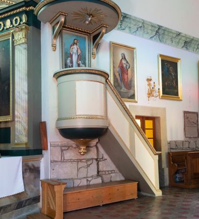 Zdjęcie nr 2: Ambona wisząca, przyścienna, z dostępem z prawej strony w postaci jednobiegowych schodów z balustradą. Kosz na planie ściętego koła, z półkolistym podwieszeniem zakończonym szyszką. Ścianka kosza i balustrada schodów zdobione płycinami w ramach. Parapet w formie gzymsu, od dołu zdobiony pasem z dekoracją roślinną. W polu zaplecka obraz z przedstawieniem Jezusa Dobrego Pasterza, ujęty ramą o dekoracji geometrycznej. Baldachim na planie ściętego koła, podtrzymywany przez dwa wsporniki, o kanelowanej krawędzi, zakończone wolutami. Brzeg baldachimu w formie gzymsu dekorowanego pasem ornamentu roślinnego. Na nim rzeźbiona skała, na której znajdują się tablice prawa. Na podniebieniu gołębica Ducha Świętego w glorii promienistej. Struktura malowana w kolorze seledynowym, płyciny kremowym, detale ciemnozielonym, profile złocone. 