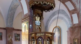 Zdjęcie nr 1: Ambona przyścienna, ustawiona na niskim filarze, dostępna od prawej strony schodami umieszczonymi przy filarze międzynawowym. Filar czworoboczny, na profilowanym cokole, naroża opięte filarkami o czworobocznych trzonach, zamknięty prostym gzymsem. Na ściankach płytkie płyciny w kształcie prostokąta o wklęsłych narożach, w złoconych obramieniach. Gzyms zdobiony rzędem niskich ostrosłupów ozdobionych rzeźbionym i złoconym greckim krzyżykiem. Filar wspiera kosz na rzucie siedmioboku, opięty na narożach kolumienkami wspierającymi belkowanie i gzyms. Ścianki kosza zdobione prostokątnymi niszami zamkniętymi łukiem półkolistym nadwieszonym. Nad niszami fryz zdobiony analogicznie jak w podstawie ambony ostrosłupami z krzyżykami greckimi, poniżej fryz z motywów rybiej łuski. We niszach, na wysokich postumentach ustawione rzeźby od lewej: kielich, św. Jan, św. Łukasz, św. Marek i św. Mateusz. Kolumny o gładkich, złoconych trzonach i kapitelach kompozytowych. Parapet w formie prostego gzymsu. Zaplecek wysoki, z płyciną zamkniętą łukiem półkolistym nadwieszonym. W polu płaskorzeźbione tablice Dekalogu umieszczone na obłokach, otoczone sześcioma wiązkami promieni o nierównej długości. Belkowanie zdobione analogicznie jak na koszu. Baldachim na rzucie ośmioboku, w formie ostrosłupa, z wydzielonym cokołem, podzielony na dwie strefy, zwieńczony umieszczonym na niskim cokole krzyżem łacińskim z odchodzącymi ze skrzyżowania ramion grubymi promieniami. Cokół baldachimu ozdobiony nad narożnikami małymi wazonikami na wysokich postumentach oraz podwieszonym lambrekinem z liści akantu. Na podniebieniu rzeźbiona Gołębica Ducha Świętego otoczona wiązkami promieni nierównej długości. Ewangeliści w niszach ukazani w pozycji stojącej, ubrani w długie i złocone szaty. Twarze szerokie, z małymi i wąskimi ustami, włosy średniej długości, ciemnobrązowe. Wokół głów złote i koliste nimby. Św. Jan zwrócony en trois quarts w lewo, z otwartą księgą Pisma Świętego w lewej dłoni, w której napis: A SŁOWO BYŁO U BOGA / I BOGIEM BYŁO SŁOWO. Św. Łukasz ukazany en face, z głową zwróconą w lewo. Św. Marek ukazany en face, z głową zwróconą w prawo. Po jego prawej stronie kolumna. Św. Mateusz ukazany frontalnie z otwartą księgą w dłoni, w tle, po jego prawej stronie drzewo. Z prawej strony jednobiegowe schody z balustradą zakończoną słupkiem w formie filaru, z arkadami zamkniętymi łukiem półkolistym. Struktura malowana w kolorze jasnobrązowym, profile i ornamenty złocone oraz srebrzone.