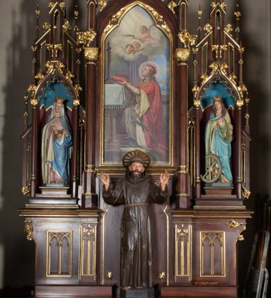 Zdjęcie nr 1: Nastawa architektoniczna, trójosiowa, jednokondygnacyjna ze zwieńczeniem, ustawiona na wysokiej predelli. Ołtarz w formie płytkiej skrzyni ustawionej na stopniu, dekorowanej z przodu dwiema półkolumienkami oraz trzema płycinami – dwiema z blendami i środkowej z godłem franciszkańskim. Mensa drewniana, wysunięta do przodu, wsparta na dwóch kolumnach. Predella dekorowana płycinami z blendami. Na jej tle, na mensie stoi figura św. Franciszka. Osie nastawy wydzielone trzema parami kolumienek podtrzymujących wimpergi z pinaklami, zakończone szczytami. Oś środkowa najwyższa, w jej polu obraz św. Ludwika w formie stojącego prostokąta zamkniętego łukiem trójlistnym ostrym, w prostej ramie dekorowanej na łuku ornamentem roślinnym. Zakończona szczytem w formie wieżyczki z przyporami i z ażurowymi blendami, zwieńczonej pinaklami dekorowanymi kwiatonami. Na osiach bocznych nisze z figurami św. Elżbiety i św. Katarzyny Aleksandryjskiej; flankowane ażurowymi blendami i maswerkami, po zewnętrznej stronie z pinaklami. Osie zakończone szczytami w formie wieżyczek z przyporami i ażurowymi blendami oraz pinaklami dekorowanymi kwiatonami. 
Struktura nastawy pokryta ciemnobrązową politurą, ornamentyka i profile złocone, wnętrza nisz polichromowane w kolorze czerwonym i niebieskim. 
