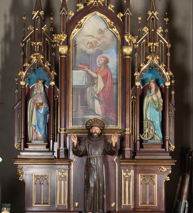 Zdjęcie nr 2: Nastawa architektoniczna, trójosiowa, jednokondygnacyjna ze zwieńczeniem, ustawiona na wysokiej predelli. Ołtarz w formie płytkiej skrzyni ustawionej na stopniu, dekorowanej z przodu dwiema półkolumienkami oraz trzema płycinami – dwiema z blendami i środkowej z godłem franciszkańskim. Mensa drewniana, wysunięta do przodu, wsparta na dwóch kolumnach. Predella dekorowana płycinami z blendami. Na jej tle, na mensie stoi figura św. Franciszka. Osie nastawy wydzielone trzema parami kolumienek podtrzymujących wimpergi z pinaklami, zakończone szczytami. Oś środkowa najwyższa, w jej polu obraz św. Ludwika w formie stojącego prostokąta zamkniętego łukiem trójlistnym ostrym, w prostej ramie dekorowanej na łuku ornamentem roślinnym. Zakończona szczytem w formie wieżyczki z przyporami i z ażurowymi blendami, zwieńczonej pinaklami dekorowanymi kwiatonami. Na osiach bocznych nisze z figurami św. Elżbiety i św. Katarzyny Aleksandryjskiej; flankowane ażurowymi blendami i maswerkami, po zewnętrznej stronie z pinaklami. Osie zakończone szczytami w formie wieżyczek z przyporami i ażurowymi blendami oraz pinaklami dekorowanymi kwiatonami. 
Struktura nastawy pokryta ciemnobrązową politurą, ornamentyka i profile złocone, wnętrza nisz polichromowane w kolorze czerwonym i niebieskim. 
