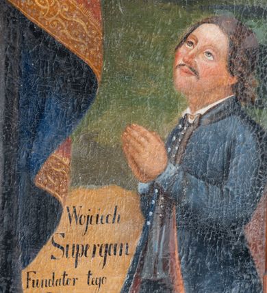 Zdjęcie nr 2: Obraz w formie stojącego prostokąta zamkniętego łukiem odcinkowym nadwieszonym z przedstawieniem św. Wojciecha ukazanego w całej postaci. Święty zwrócony jest w trzech czwartych w lewo, w prawej, uniesionej ręce trzyma laskę zakończoną krzyżem patriarchalnym, lewą, ugiętą przytrzymuje przy boku księgę. Twarz ma pociągłą, szczupłą, o starczych rysach, z migdałowatymi oczami, garbatym nosem i wąskimi ustami; okoloną długą, białą brodą oraz siwymi włosami sięgającymi ramion. Ubrany jest w czarną albę, białą rokietę, lamowaną koronką oraz czerwoną kapę ze złoconą bordiurą i niebieską podszewką, zapiętą na piersi klamrą. Na piersi ma paliusz, na głowie czerwoną infułę z wizerunkiem gołębicy Ducha Świętego. Po prawej stronie świętego stoi anioł w zielonej tunice, który w lewej ręce trzyma wiosło, prawą wskazuje na nie. Po lewej stronie świętego, w rogu, klęcząca półpostać fundatora z dłońmi złożonymi w geście modlitwy. Mężczyzna nosi wąsy, włosy ma zawiązane z tyłu głowy, ubrany jest w kamizelkę oraz habit à la française. Przed nim znajduje się kartusz z napisem „Wojciech / Supergan / Fundator tego / Ołtarza / A(nno) D(omini) 1800”. Po tej samej stronie w oddali ukazany kościół św. Wojciecha z Krakowa. W górnej części obrazu wyobrażone niebo z obłokami, pośród których po prawej stronie świętego znajduje się putto trzymające liść palmy, a wokół głowy Wojciecha pięć uskrzydlonych główek anielskich. 