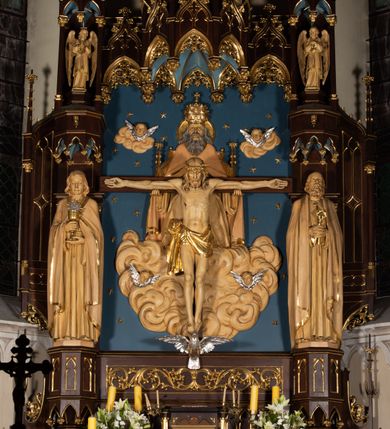 Zdjęcie nr 19: Nastawa architektoniczna, jednoosiowa, jednokondygnacyjna, ze zwieńczeniem, ustawiona na wysokim cokole. Ołtarz ustawiony na pięciostopniowej kamiennej podstawie; granitowy, prostopadłościenny, z monogramem IHS na froncie, mensa granitowa. Na nim drewniane tabernakulum w formie prostopadłościennej skrzynki, flankowane parą kolumienek, zamknięte od góry profilowanym gzymsem. Na ściance frontowej wysunięte do przodu metalowe drzwiczki w oprawie architektonicznej na niskim cokole, zamknięte od góry prostym gzymsem. Na drzwiczkach kielich z hostią, w płycinie o kształcie prostokąta stojącego zamkniętego łukiem trójlistnym ostrym. 
Nastawa flankowana dwiema dwukondygnacyjnymi wieżyczkami na planie ośmioboku z figurami św. Jana Ewangelisty i św. Piotra w pierwszej kondygnacji oraz figurami aniołów w drugiej. Figury apostołów ustawione są na ośmiobocznych wspornikach zdobionych od dołu arkadowaniem z kwiatonami, podtrzymywanych przez ośmioboczne kolumienki, flankujące kamienny ołtarz. Nad figurami ośmioboczne baldachimy zdobione od dołu arkadowaniem z kwiatonami, stanowiące podstawę dla figur aniołów, które zwieńczone są analogicznymi ośmiobocznymi baldachimami i rozbudowanymi pinaklami. W polu środkowym rzeźbiona Trójca Święta ukazana jako Tron łaski pośród obłoków i uskrzydlonych główek anielskich. Nad nią duży, ośmioboczny baldachim, zdobiony od dołu arkadowaniem, zakończonym kwiatonami, dekorowany maswerkami, wimpergami i kwiatonami, naprzemiennie z pinaklami, który stanowi podstawę wieżyczki wieńczącej ołtarz. W jej polu ustawiona figura Matki Boskiej, nad nią ośmioboczny baldachim zdobiony od dołu arkadowaniem i kwiatonami, zakończony dużym pinaklem dekorowanym żabkami. Nastawa flankowana uszami w formie przypór dekorowanych maswerkiem i wąskimi kolumienkami z pinaklami. 
Struktura politurowana w kolorze ciemnobrązowym, detale i ornamentyka złocone, tło pola głównego oraz podniebienia baldachimów błękitne.