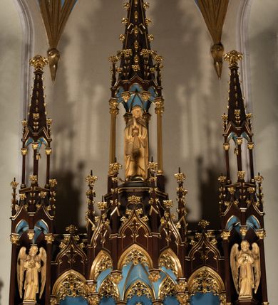 Zdjęcie nr 20: Nastawa architektoniczna, jednoosiowa, jednokondygnacyjna, ze zwieńczeniem, ustawiona na wysokim cokole. Ołtarz ustawiony na pięciostopniowej kamiennej podstawie; granitowy, prostopadłościenny, z monogramem IHS na froncie, mensa granitowa. Na nim drewniane tabernakulum w formie prostopadłościennej skrzynki, flankowane parą kolumienek, zamknięte od góry profilowanym gzymsem. Na ściance frontowej wysunięte do przodu metalowe drzwiczki w oprawie architektonicznej na niskim cokole, zamknięte od góry prostym gzymsem. Na drzwiczkach kielich z hostią, w płycinie o kształcie prostokąta stojącego zamkniętego łukiem trójlistnym ostrym. 
Nastawa flankowana dwiema dwukondygnacyjnymi wieżyczkami na planie ośmioboku z figurami św. Jana Ewangelisty i św. Piotra w pierwszej kondygnacji oraz figurami aniołów w drugiej. Figury apostołów ustawione są na ośmiobocznych wspornikach zdobionych od dołu arkadowaniem z kwiatonami, podtrzymywanych przez ośmioboczne kolumienki, flankujące kamienny ołtarz. Nad figurami ośmioboczne baldachimy zdobione od dołu arkadowaniem z kwiatonami, stanowiące podstawę dla figur aniołów, które zwieńczone są analogicznymi ośmiobocznymi baldachimami i rozbudowanymi pinaklami. W polu środkowym rzeźbiona Trójca Święta ukazana jako Tron łaski pośród obłoków i uskrzydlonych główek anielskich. Nad nią duży, ośmioboczny baldachim, zdobiony od dołu arkadowaniem, zakończonym kwiatonami, dekorowany maswerkami, wimpergami i kwiatonami, naprzemiennie z pinaklami, który stanowi podstawę wieżyczki wieńczącej ołtarz. W jej polu ustawiona figura Matki Boskiej, nad nią ośmioboczny baldachim zdobiony od dołu arkadowaniem i kwiatonami, zakończony dużym pinaklem dekorowanym żabkami. Nastawa flankowana uszami w formie przypór dekorowanych maswerkiem i wąskimi kolumienkami z pinaklami. 
Struktura politurowana w kolorze ciemnobrązowym, detale i ornamentyka złocone, tło pola głównego oraz podniebienia baldachimów błękitne.