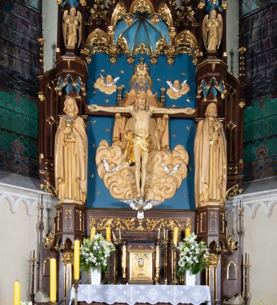 Zdjęcie nr 1: Nastawa architektoniczna, jednoosiowa, jednokondygnacyjna, ze zwieńczeniem, ustawiona na wysokim cokole. Ołtarz ustawiony na pięciostopniowej kamiennej podstawie; granitowy, prostopadłościenny, z monogramem IHS na froncie, mensa granitowa. Na nim drewniane tabernakulum w formie prostopadłościennej skrzynki, flankowane parą kolumienek, zamknięte od góry profilowanym gzymsem. Na ściance frontowej wysunięte do przodu metalowe drzwiczki w oprawie architektonicznej na niskim cokole, zamknięte od góry prostym gzymsem. Na drzwiczkach kielich z hostią, w płycinie o kształcie prostokąta stojącego zamkniętego łukiem trójlistnym ostrym. 
Nastawa flankowana dwiema dwukondygnacyjnymi wieżyczkami na planie ośmioboku z figurami św. Jana Ewangelisty i św. Piotra w pierwszej kondygnacji oraz figurami aniołów w drugiej. Figury apostołów ustawione są na ośmiobocznych wspornikach zdobionych od dołu arkadowaniem z kwiatonami, podtrzymywanych przez ośmioboczne kolumienki, flankujące kamienny ołtarz. Nad figurami ośmioboczne baldachimy zdobione od dołu arkadowaniem z kwiatonami, stanowiące podstawę dla figur aniołów, które zwieńczone są analogicznymi ośmiobocznymi baldachimami i rozbudowanymi pinaklami. W polu środkowym rzeźbiona Trójca Święta ukazana jako Tron łaski pośród obłoków i uskrzydlonych główek anielskich. Nad nią duży, ośmioboczny baldachim, zdobiony od dołu arkadowaniem, zakończonym kwiatonami, dekorowany maswerkami, wimpergami i kwiatonami, naprzemiennie z pinaklami, który stanowi podstawę wieżyczki wieńczącej ołtarz. W jej polu ustawiona figura Matki Boskiej, nad nią ośmioboczny baldachim zdobiony od dołu arkadowaniem i kwiatonami, zakończony dużym pinaklem dekorowanym żabkami. Nastawa flankowana uszami w formie przypór dekorowanych maswerkiem i wąskimi kolumienkami z pinaklami. 
Struktura politurowana w kolorze ciemnobrązowym, detale i ornamentyka złocone, tło pola głównego oraz podniebienia baldachimów błękitne.