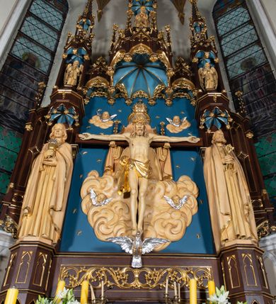 Zdjęcie nr 18: Nastawa architektoniczna, jednoosiowa, jednokondygnacyjna, ze zwieńczeniem, ustawiona na wysokim cokole. Ołtarz ustawiony na pięciostopniowej kamiennej podstawie; granitowy, prostopadłościenny, z monogramem IHS na froncie, mensa granitowa. Na nim drewniane tabernakulum w formie prostopadłościennej skrzynki, flankowane parą kolumienek, zamknięte od góry profilowanym gzymsem. Na ściance frontowej wysunięte do przodu metalowe drzwiczki w oprawie architektonicznej na niskim cokole, zamknięte od góry prostym gzymsem. Na drzwiczkach kielich z hostią, w płycinie o kształcie prostokąta stojącego zamkniętego łukiem trójlistnym ostrym. 
Nastawa flankowana dwiema dwukondygnacyjnymi wieżyczkami na planie ośmioboku z figurami św. Jana Ewangelisty i św. Piotra w pierwszej kondygnacji oraz figurami aniołów w drugiej. Figury apostołów ustawione są na ośmiobocznych wspornikach zdobionych od dołu arkadowaniem z kwiatonami, podtrzymywanych przez ośmioboczne kolumienki, flankujące kamienny ołtarz. Nad figurami ośmioboczne baldachimy zdobione od dołu arkadowaniem z kwiatonami, stanowiące podstawę dla figur aniołów, które zwieńczone są analogicznymi ośmiobocznymi baldachimami i rozbudowanymi pinaklami. W polu środkowym rzeźbiona Trójca Święta ukazana jako Tron łaski pośród obłoków i uskrzydlonych główek anielskich. Nad nią duży, ośmioboczny baldachim, zdobiony od dołu arkadowaniem, zakończonym kwiatonami, dekorowany maswerkami, wimpergami i kwiatonami, naprzemiennie z pinaklami, który stanowi podstawę wieżyczki wieńczącej ołtarz. W jej polu ustawiona figura Matki Boskiej, nad nią ośmioboczny baldachim zdobiony od dołu arkadowaniem i kwiatonami, zakończony dużym pinaklem dekorowanym żabkami. Nastawa flankowana uszami w formie przypór dekorowanych maswerkiem i wąskimi kolumienkami z pinaklami. 
Struktura politurowana w kolorze ciemnobrązowym, detale i ornamentyka złocone, tło pola głównego oraz podniebienia baldachimów błękitne.