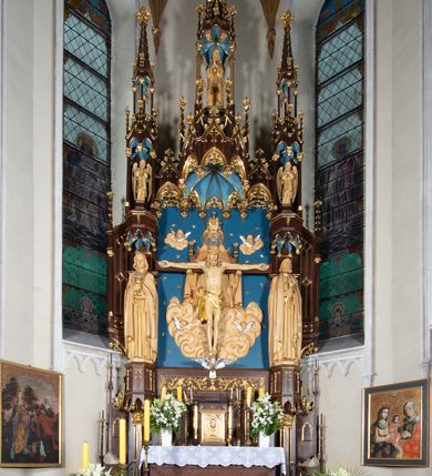 Zdjęcie nr 17: Nastawa architektoniczna, jednoosiowa, jednokondygnacyjna, ze zwieńczeniem, ustawiona na wysokim cokole. Ołtarz ustawiony na pięciostopniowej kamiennej podstawie; granitowy, prostopadłościenny, z monogramem IHS na froncie, mensa granitowa. Na nim drewniane tabernakulum w formie prostopadłościennej skrzynki, flankowane parą kolumienek, zamknięte od góry profilowanym gzymsem. Na ściance frontowej wysunięte do przodu metalowe drzwiczki w oprawie architektonicznej na niskim cokole, zamknięte od góry prostym gzymsem. Na drzwiczkach kielich z hostią, w płycinie o kształcie prostokąta stojącego zamkniętego łukiem trójlistnym ostrym. 
Nastawa flankowana dwiema dwukondygnacyjnymi wieżyczkami na planie ośmioboku z figurami św. Jana Ewangelisty i św. Piotra w pierwszej kondygnacji oraz figurami aniołów w drugiej. Figury apostołów ustawione są na ośmiobocznych wspornikach zdobionych od dołu arkadowaniem z kwiatonami, podtrzymywanych przez ośmioboczne kolumienki, flankujące kamienny ołtarz. Nad figurami ośmioboczne baldachimy zdobione od dołu arkadowaniem z kwiatonami, stanowiące podstawę dla figur aniołów, które zwieńczone są analogicznymi ośmiobocznymi baldachimami i rozbudowanymi pinaklami. W polu środkowym rzeźbiona Trójca Święta ukazana jako Tron łaski pośród obłoków i uskrzydlonych główek anielskich. Nad nią duży, ośmioboczny baldachim, zdobiony od dołu arkadowaniem, zakończonym kwiatonami, dekorowany maswerkami, wimpergami i kwiatonami, naprzemiennie z pinaklami, który stanowi podstawę wieżyczki wieńczącej ołtarz. W jej polu ustawiona figura Matki Boskiej, nad nią ośmioboczny baldachim zdobiony od dołu arkadowaniem i kwiatonami, zakończony dużym pinaklem dekorowanym żabkami. Nastawa flankowana uszami w formie przypór dekorowanych maswerkiem i wąskimi kolumienkami z pinaklami. 
Struktura politurowana w kolorze ciemnobrązowym, detale i ornamentyka złocone, tło pola głównego oraz podniebienia baldachimów błękitne.