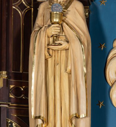 Zdjęcie nr 12: Nastawa architektoniczna, jednoosiowa, jednokondygnacyjna, ze zwieńczeniem, ustawiona na wysokim cokole. Ołtarz ustawiony na pięciostopniowej kamiennej podstawie; granitowy, prostopadłościenny, z monogramem IHS na froncie, mensa granitowa. Na nim drewniane tabernakulum w formie prostopadłościennej skrzynki, flankowane parą kolumienek, zamknięte od góry profilowanym gzymsem. Na ściance frontowej wysunięte do przodu metalowe drzwiczki w oprawie architektonicznej na niskim cokole, zamknięte od góry prostym gzymsem. Na drzwiczkach kielich z hostią, w płycinie o kształcie prostokąta stojącego zamkniętego łukiem trójlistnym ostrym. 
Nastawa flankowana dwiema dwukondygnacyjnymi wieżyczkami na planie ośmioboku z figurami św. Jana Ewangelisty i św. Piotra w pierwszej kondygnacji oraz figurami aniołów w drugiej. Figury apostołów ustawione są na ośmiobocznych wspornikach zdobionych od dołu arkadowaniem z kwiatonami, podtrzymywanych przez ośmioboczne kolumienki, flankujące kamienny ołtarz. Nad figurami ośmioboczne baldachimy zdobione od dołu arkadowaniem z kwiatonami, stanowiące podstawę dla figur aniołów, które zwieńczone są analogicznymi ośmiobocznymi baldachimami i rozbudowanymi pinaklami. W polu środkowym rzeźbiona Trójca Święta ukazana jako Tron łaski pośród obłoków i uskrzydlonych główek anielskich. Nad nią duży, ośmioboczny baldachim, zdobiony od dołu arkadowaniem, zakończonym kwiatonami, dekorowany maswerkami, wimpergami i kwiatonami, naprzemiennie z pinaklami, który stanowi podstawę wieżyczki wieńczącej ołtarz. W jej polu ustawiona figura Matki Boskiej, nad nią ośmioboczny baldachim zdobiony od dołu arkadowaniem i kwiatonami, zakończony dużym pinaklem dekorowanym żabkami. Nastawa flankowana uszami w formie przypór dekorowanych maswerkiem i wąskimi kolumienkami z pinaklami. 
Struktura politurowana w kolorze ciemnobrązowym, detale i ornamentyka złocone, tło pola głównego oraz podniebienia baldachimów błękitne.