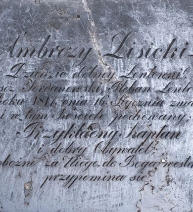 Zdjęcie nr 1: Epitafium w formie leżącego prostokąta, w narożach metalowe śluby. W polu inskrypcja „Ambroży Lisicki / Dziedzic dólnéy Łentowni, / Proboszcz Jordanowski, Pleban Łentowski, / w Roku 1817. Dnia 16. Stycznia zmarły, / i w tym Kościele pochowany; / Przykładny Kapłan / i dobry Obywatel; / o pobożne za Niego, do Boga westchnienie, / przypomina się.”