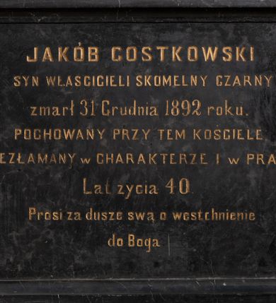 Zdjęcie nr 1: Epitafium w formie leżącego prostokąta, ujęte profilowaną ramą oraz złoconą, drewnianą ramą. W narożach cztery śruby. W polu złocona inskrypcja: „JAKÓB GOSTKOWSKI / SYN WŁASCICIELI SKOMELNY CZARNY / zmarł 31 Grudnia 1892 roku. / POCHOWANY PRZY TEM KOŚCIELE. / NIEZŁAMANY w CHARAKTERZE I w PRACY. / Lat życia 40. / Prosi za dusze swą o westchnienie / do Boga”.