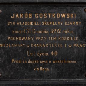 Zdjęcie nr 1: Epitafium w formie leżącego prostokąta, ujęte profilowaną ramą oraz złoconą, drewnianą ramą. W narożach cztery śruby. W polu złocona inskrypcja: „JAKÓB GOSTKOWSKI / SYN WŁASCICIELI SKOMELNY CZARNY / zmarł 31 Grudnia 1892 roku. / POCHOWANY PRZY TEM KOŚCIELE. / NIEZŁAMANY w CHARAKTERZE I w PRACY. / Lat życia 40. / Prosi za dusze swą o westchnienie / do Boga”.