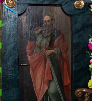 Zdjęcie nr 3: Obraz w formie stojącego prostokąta o wklęsłych górnych narożach z przedstawieniem św. Pawła. Apostoł ukazany w całej postaci, zwrócony w trzech czwartych w prawo, w kontrapoście, lewą ręką przytrzymuje przy boku księgę oraz miecz skierowany ostrzem w dół, prawą rękę unosi w geście błogosławieństwa. Twarz ma pociągłą, z wysokim czołem, o dużych, migdałowatych oczach, garbatym nosie i małych ustach, okoloną gęstą, długą, kręconą brodą i krótkimi włosami. Wokół głowy ma nimb. Ubrany jest w jasnozieloną tunikę z kołnierzykiem, przepasaną w talii oraz jasnoczerwony płaszcz narzucony na ramiona i zawiązany z przodu postaci. Święty ukazany na cieniowanym, brązowym tle, z widocznym u dołu jasnobrązowym podłożem. 