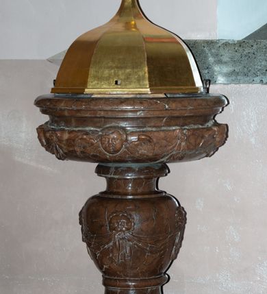 Zdjęcie nr 2: Chrzcielnica kielichowa, ustawiona na dużej podstawie na rzucie ściętego koła oraz na prostopadłościennym cokole na rzucie kwadratu. Trzon wklęsło-wypukły z uskokiem u spodu; nodus gruszkowaty, dekorowany czterema lwimi głowami trzymającymi w paszczach festony z podwieszonej tkaniny. Czara w formie bardzo spłaszczonej półkuli z wywiniętą i profilowaną krawędzią; dekorowana uskrzydlonymi główkami anielskimi na przemian z kokardami z podwieszonymi festonami z tkaniny. Pokrywa w formie baldachimu na rzucie sześcioboku, wypiętrzona, zwieńczona krzyżem.