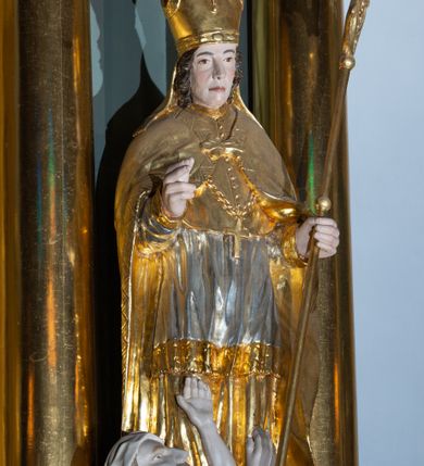 Zdjęcie nr 8: Ołtarz architektoniczny, jednoosiowy, z wydzieloną częścią cokołową i predellą, jednokondygnacyjny, ze zwieńczeniem, dostępny po dwóch kamiennych stopniach. Mensa drewniana z kamiennym portatylem, wsparta na tumbie z neorokokowym kartuszem na froncie. Tabernakulum w formie prostopadłościennej skrzynki, flankowanej z przodu płaskorzeźbionymi kolumienkami, nad nimi rozety; górna krawędź obwiedziona profilowanym gzymsem. Drzwiczki w kształcie formie stojącego prostokąta zamkniętego łukiem półkolistym nadwieszonym, ujęte ramą, z płaskorzeźbionym przedstawieniem kielicha i hostii w polu. Nastawa ujęta dwiema parami kolumn umieszczonych na tle pilastrów podtrzymujących pełne belkowanie, przerwane nad polem środkowym, występujące ponad kolumnami; skrajna para kolumn ustawiona ukośnie względem retabulum. W polu środkowym nisza w kształcie stojącego prostokąta zamkniętego łukiem wklęsło-wypukłym nadwieszonym, ujęta podwójną profilowaną ramą, w niszy obraz Trójcą Święta. Ponad obrazem, na osin neorokokowy kartusz z koroną i inicjałami: KK, otoczony czterema uskrzydlonymi główkami anielskimi. Pomiędzy kolumnami figury św. Wojciecha i św. Stanisława ustawione na konsolach. Zwieńczenie w kształcie aedikuli, ujęte parą łukowato wygiętych pilastrów oraz spływami wolutowymi, na gzymsie koronującym z płaskorzeźbionym Okiem Opatrzności w glorii promienistej oraz z parą wazonów po bokach. W polu owalny obraz z przedstawieniem Ecce Homo ujęty profilowaną ramą. W zwieńczeniu, w osiach kolumn para puttów i para wazonów. Trzony pilastrów i przyłucza w polu głównym dekorowane ornamentem neorokokowym; fryz zdobiony rozetami. Struktura polichromowana w kolorze seledynowym; kolumny, ornamenty i profile złocone.