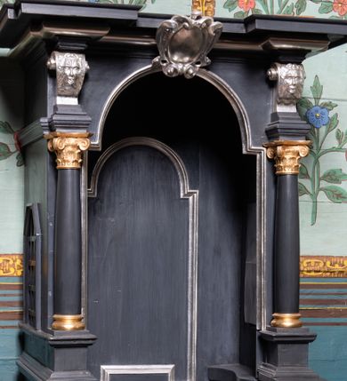 Zdjęcie nr 1: Konfesjonał ustawiony na niskiej podstawie z klęcznikami. Złożony z siedziska z wysokim zapleckiem, zakończonym płaskim baldachimem. Siedzisko ujęte dwiema wysokimi ściankami bocznymi, w połowie wysokości zwężonymi, od frontu z otworem w formie stojącego prostokąta zamkniętego łukiem półkolistym nadwieszonym, z przedpiersiem w postaci niskich drzwiczek. Dolna połowa konfesjonału zwieńczona gzymsem, ścianki dekorowane płycinami w kształcie prostokątów i rombu. W górnej połowie otwór ścianki frontowej ujęty kolumienkami na cokołach, dźwigającymi konsole z maszkaronami, podtrzymującymi gzyms obiegający wszystkie boki konfesjonału, wyłamany w narożach. W partii gzymsu, nad otworem frontowym kartusz. Na ściankach bocznych prześwity z kratką. Zaplecek dekorowany płyciną w formie stojącego prostokąta zamkniętego łukiem półkolistym nadwieszonym. Struktura polichromowana w kolorze czarnym, profilowania i dekoracja srebrzone, detale złocone. 