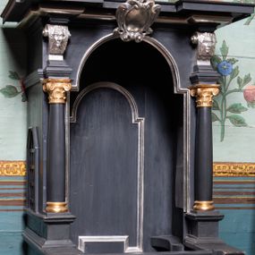 Zdjęcie nr 1: Konfesjonał ustawiony na niskiej podstawie z klęcznikami. Złożony z siedziska z wysokim zapleckiem, zakończonym płaskim baldachimem. Siedzisko ujęte dwiema wysokimi ściankami bocznymi, w połowie wysokości zwężonymi, od frontu z otworem w formie stojącego prostokąta zamkniętego łukiem półkolistym nadwieszonym, z przedpiersiem w postaci niskich drzwiczek. Dolna połowa konfesjonału zwieńczona gzymsem, ścianki dekorowane płycinami w kształcie prostokątów i rombu. W górnej połowie otwór ścianki frontowej ujęty kolumienkami na cokołach, dźwigającymi konsole z maszkaronami, podtrzymującymi gzyms obiegający wszystkie boki konfesjonału, wyłamany w narożach. W partii gzymsu, nad otworem frontowym kartusz. Na ściankach bocznych prześwity z kratką. Zaplecek dekorowany płyciną w formie stojącego prostokąta zamkniętego łukiem półkolistym nadwieszonym. Struktura polichromowana w kolorze czarnym, profilowania i dekoracja srebrzone, detale złocone. 