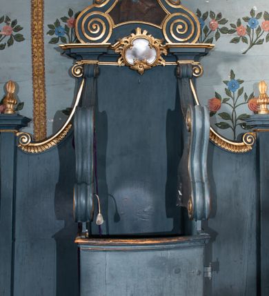 Zdjęcie nr 1: Konfesjonał ustawiony na dwustopniowej podstawie na planie półowalu. Złożony z siedziska z wysokim zapleckiem, zakończonym gzymsem wyłamanym po bokach, dekorowanym kartuszem, ze zwieńczeniem. Siedzisko ujęte dwiema ściankami bocznymi, w górnej połowie przyjmującymi fantazyjną formę rysowaną przez spływy wolutowe, z prześwitami z kratownicą. W partii przedpiersia wypukłe drzwiczki zakończone profilowanym gzymsem. Zaplecek ujęty dwiema ściankami tylnymi w formie spływów wolutowych opadających na półfilary z wazonikami. Zwieńczenie w kształcie zbliżonym do trapezu, flankowane przez spływy wolutowe, zamknięte fragmentem gzymsu przyjmującym formę łuku odcinkowego nadwieszonego, zwieńczonego dużą muszlą. W polu obraz św. Piotra ujęty profilowaną ramą, w kształcie zbliżonym do zwieńczenia. Struktura polichromowana w kolorze niebieskim, profile i ornamentyka złocone, detal srebrzony.