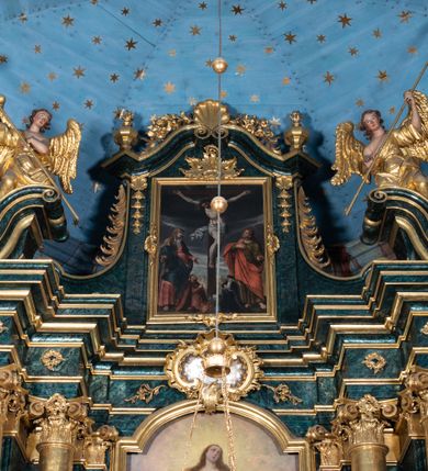 Zdjęcie nr 19: Nastawa ołtarzowa architektoniczna, jednokondygnacyjna ze zwieńczeniem, jednoosiowa z bramkami. Ołtarz prostopadłościenny, murowany, w drewnianej obudowie, z drewnianą mensą. Antepedium ujęte profilowaną ramą; w polu malowana płycina w formie leżącego prostokąta o zaokrąglonych narożach, wypełniona gałązkami różanymi, z akantowo-regencyjnym kartuszem. W narożach antepedium malowane ptaki siedzące na gałązkach. W polu kartusza ukazana scena męczeństwa św. Szymona i św. Judy Tadeusza, na tle pejzażu. Tabernakulum metalowe, prostopadłościenne, flankowane pilastrami w formie spływów wolutowych zdobionych gałązkami róży, zamknięte od góry profilowanym gzymsem. Drzwiczki w kształcie stojącego prostokąta zamkniętego łukiem odcinkowym nadwieszonym; w polu przedstawienie kielicha z hostią. Tabernakulum wprawione w wysoki cokół, na którym stoi tron wystawienia w formie obrotowej niszy, o wypukłej ściance frontowej i ustawionymi pod kątem ściankami bocznymi. Nisza flankowana parą kolumienek i spływów wolutowych dźwigających belkowanie oraz fragmenty przerwanego, półkolistego przyczółka. Na belkowaniu szczyt z rocaillem, z napisem w polu: „ECCE / TABERNACULUM / DEI”. Nastawa ustawiona na dwustrefowym cokole, z wyodrębnionymi czterema prostopadłościanami, w górnej części zdobionym płycinami. Retabulum ujęte parami pilastrów i filarów o kanelowanych trzonach oraz stojącymi przed nimi w układzie schodkowym kolumnami o kapitelach kompozytowych. Podpory dźwigają pełne belkowanie, wyłamane na ich osi, z przerwanym architrawem nad polem środkowym. Na belkowaniu fragmenty falistego, przerwanego przyczółka z figurami aniołów z arma Christi. W polu środkowym wnęka w formie stojącego prostokąta zamkniętego łukiem odcinkowym nadwieszonym, ujęta profilowaną ramą, z obrazem Najświętszej Marii Panny Niepokalanie Poczętej. Nad nią, w polu belkowania rocaille'owy kartusz z napisem „HI / SUNT VIRI / MISERICORDIAE / [...]ccdis 44”. Zwieńczenie w formie zbliżonej do stojącego prostokąta, ujętego pilastrami przechodzącymi w spływy wolutowe, zamkniętego dwoma fragmentami wolutowego gzymsu. Całość zakończona szczytem utworzonym z muszli i zwisów kwiatowych, flankowanym przez dwa wazony. Zwieńczenie ujęte liśćmi palmowymi. W polu obraz z grupą Ukrzyżowania w formie stojącego prostokąta, w profilowanej ramie, dekorowanej rocaille'm. Nastawa flankowana bramkami zwieńczonymi konsolami, na których stoją figury Marii i św. Jana Ewangelisty. Przejścia w formie stojącego prostokąta o wklęsłych górnych narożach, z drzwiczkami z malowanymi przedstawieniami św. Piotra i św. Pawła. Struktura polichromowana na sposób imitujący marmoryzację w kolorze zielono-niebieskim, z laserunkiem, kolumny, ornamentyka i profile złocone, detal srebrzony.