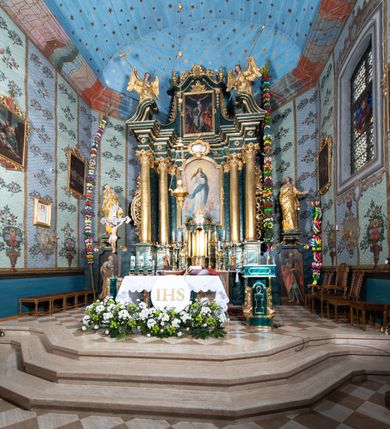 Zdjęcie nr 13: Nastawa ołtarzowa architektoniczna, jednokondygnacyjna ze zwieńczeniem, jednoosiowa z bramkami. Ołtarz prostopadłościenny, murowany, w drewnianej obudowie, z drewnianą mensą. Antepedium ujęte profilowaną ramą; w polu malowana płycina w formie leżącego prostokąta o zaokrąglonych narożach, wypełniona gałązkami różanymi, z akantowo-regencyjnym kartuszem. W narożach antepedium malowane ptaki siedzące na gałązkach. W polu kartusza ukazana scena męczeństwa św. Szymona i św. Judy Tadeusza, na tle pejzażu. Tabernakulum metalowe, prostopadłościenne, flankowane pilastrami w formie spływów wolutowych zdobionych gałązkami róży, zamknięte od góry profilowanym gzymsem. Drzwiczki w kształcie stojącego prostokąta zamkniętego łukiem odcinkowym nadwieszonym; w polu przedstawienie kielicha z hostią. Tabernakulum wprawione w wysoki cokół, na którym stoi tron wystawienia w formie obrotowej niszy, o wypukłej ściance frontowej i ustawionymi pod kątem ściankami bocznymi. Nisza flankowana parą kolumienek i spływów wolutowych dźwigających belkowanie oraz fragmenty przerwanego, półkolistego przyczółka. Na belkowaniu szczyt z rocaillem, z napisem w polu: „ECCE / TABERNACULUM / DEI”. Nastawa ustawiona na dwustrefowym cokole, z wyodrębnionymi czterema prostopadłościanami, w górnej części zdobionym płycinami. Retabulum ujęte parami pilastrów i filarów o kanelowanych trzonach oraz stojącymi przed nimi w układzie schodkowym kolumnami o kapitelach kompozytowych. Podpory dźwigają pełne belkowanie, wyłamane na ich osi, z przerwanym architrawem nad polem środkowym. Na belkowaniu fragmenty falistego, przerwanego przyczółka z figurami aniołów z arma Christi. W polu środkowym wnęka w formie stojącego prostokąta zamkniętego łukiem odcinkowym nadwieszonym, ujęta profilowaną ramą, z obrazem Najświętszej Marii Panny Niepokalanie Poczętej. Nad nią, w polu belkowania rocaille'owy kartusz z napisem „HI / SUNT VIRI / MISERICORDIAE / [...]ccdis 44”. Zwieńczenie w formie zbliżonej do stojącego prostokąta, ujętego pilastrami przechodzącymi w spływy wolutowe, zamkniętego dwoma fragmentami wolutowego gzymsu. Całość zakończona szczytem utworzonym z muszli i zwisów kwiatowych, flankowanym przez dwa wazony. Zwieńczenie ujęte liśćmi palmowymi. W polu obraz z grupą Ukrzyżowania w formie stojącego prostokąta, w profilowanej ramie, dekorowanej rocaille'm. Nastawa flankowana bramkami zwieńczonymi konsolami, na których stoją figury Marii i św. Jana Ewangelisty. Przejścia w formie stojącego prostokąta o wklęsłych górnych narożach, z drzwiczkami z malowanymi przedstawieniami św. Piotra i św. Pawła. Struktura polichromowana na sposób imitujący marmoryzację w kolorze zielono-niebieskim, z laserunkiem, kolumny, ornamentyka i profile złocone, detal srebrzony.