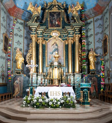 Zdjęcie nr 35: Nastawa ołtarzowa architektoniczna, jednokondygnacyjna ze zwieńczeniem, jednoosiowa z bramkami. Ołtarz prostopadłościenny, murowany, w drewnianej obudowie, z drewnianą mensą. Antepedium ujęte profilowaną ramą; w polu malowana płycina w formie leżącego prostokąta o zaokrąglonych narożach, wypełniona gałązkami różanymi, z akantowo-regencyjnym kartuszem. W narożach antepedium malowane ptaki siedzące na gałązkach. W polu kartusza ukazana scena męczeństwa św. Szymona i św. Judy Tadeusza, na tle pejzażu. Tabernakulum metalowe, prostopadłościenne, flankowane pilastrami w formie spływów wolutowych zdobionych gałązkami róży, zamknięte od góry profilowanym gzymsem. Drzwiczki w kształcie stojącego prostokąta zamkniętego łukiem odcinkowym nadwieszonym; w polu przedstawienie kielicha z hostią. Tabernakulum wprawione w wysoki cokół, na którym stoi tron wystawienia w formie obrotowej niszy, o wypukłej ściance frontowej i ustawionymi pod kątem ściankami bocznymi. Nisza flankowana parą kolumienek i spływów wolutowych dźwigających belkowanie oraz fragmenty przerwanego, półkolistego przyczółka. Na belkowaniu szczyt z rocaillem, z napisem w polu: „ECCE / TABERNACULUM / DEI”. Nastawa ustawiona na dwustrefowym cokole, z wyodrębnionymi czterema prostopadłościanami, w górnej części zdobionym płycinami. Retabulum ujęte parami pilastrów i filarów o kanelowanych trzonach oraz stojącymi przed nimi w układzie schodkowym kolumnami o kapitelach kompozytowych. Podpory dźwigają pełne belkowanie, wyłamane na ich osi, z przerwanym architrawem nad polem środkowym. Na belkowaniu fragmenty falistego, przerwanego przyczółka z figurami aniołów z arma Christi. W polu środkowym wnęka w formie stojącego prostokąta zamkniętego łukiem odcinkowym nadwieszonym, ujęta profilowaną ramą, z obrazem Najświętszej Marii Panny Niepokalanie Poczętej. Nad nią, w polu belkowania rocaille'owy kartusz z napisem „HI / SUNT VIRI / MISERICORDIAE / [...]ccdis 44”. Zwieńczenie w formie zbliżonej do stojącego prostokąta, ujętego pilastrami przechodzącymi w spływy wolutowe, zamkniętego dwoma fragmentami wolutowego gzymsu. Całość zakończona szczytem utworzonym z muszli i zwisów kwiatowych, flankowanym przez dwa wazony. Zwieńczenie ujęte liśćmi palmowymi. W polu obraz z grupą Ukrzyżowania w formie stojącego prostokąta, w profilowanej ramie, dekorowanej rocaille'm. Nastawa flankowana bramkami zwieńczonymi konsolami, na których stoją figury Marii i św. Jana Ewangelisty. Przejścia w formie stojącego prostokąta o wklęsłych górnych narożach, z drzwiczkami z malowanymi przedstawieniami św. Piotra i św. Pawła. Struktura polichromowana na sposób imitujący marmoryzację w kolorze zielono-niebieskim, z laserunkiem, kolumny, ornamentyka i profile złocone, detal srebrzony.