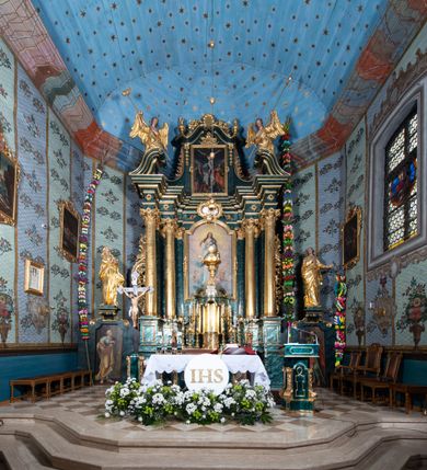 Zdjęcie nr 2: Nastawa ołtarzowa architektoniczna, jednokondygnacyjna ze zwieńczeniem, jednoosiowa z bramkami. Ołtarz prostopadłościenny, murowany, w drewnianej obudowie, z drewnianą mensą. Antepedium ujęte profilowaną ramą; w polu malowana płycina w formie leżącego prostokąta o zaokrąglonych narożach, wypełniona gałązkami różanymi, z akantowo-regencyjnym kartuszem. W narożach antepedium malowane ptaki siedzące na gałązkach. W polu kartusza ukazana scena męczeństwa św. Szymona i św. Judy Tadeusza, na tle pejzażu. Tabernakulum metalowe, prostopadłościenne, flankowane pilastrami w formie spływów wolutowych zdobionych gałązkami róży, zamknięte od góry profilowanym gzymsem. Drzwiczki w kształcie stojącego prostokąta zamkniętego łukiem odcinkowym nadwieszonym; w polu przedstawienie kielicha z hostią. Tabernakulum wprawione w wysoki cokół, na którym stoi tron wystawienia w formie obrotowej niszy, o wypukłej ściance frontowej i ustawionymi pod kątem ściankami bocznymi. Nisza flankowana parą kolumienek i spływów wolutowych dźwigających belkowanie oraz fragmenty przerwanego, półkolistego przyczółka. Na belkowaniu szczyt z rocaillem, z napisem w polu: „ECCE / TABERNACULUM / DEI”. Nastawa ustawiona na dwustrefowym cokole, z wyodrębnionymi czterema prostopadłościanami, w górnej części zdobionym płycinami. Retabulum ujęte parami pilastrów i filarów o kanelowanych trzonach oraz stojącymi przed nimi w układzie schodkowym kolumnami o kapitelach kompozytowych. Podpory dźwigają pełne belkowanie, wyłamane na ich osi, z przerwanym architrawem nad polem środkowym. Na belkowaniu fragmenty falistego, przerwanego przyczółka z figurami aniołów z arma Christi. W polu środkowym wnęka w formie stojącego prostokąta zamkniętego łukiem odcinkowym nadwieszonym, ujęta profilowaną ramą, z obrazem Najświętszej Marii Panny Niepokalanie Poczętej. Nad nią, w polu belkowania rocaille'owy kartusz z napisem „HI / SUNT VIRI / MISERICORDIAE / [...]ccdis 44”. Zwieńczenie w formie zbliżonej do stojącego prostokąta, ujętego pilastrami przechodzącymi w spływy wolutowe, zamkniętego dwoma fragmentami wolutowego gzymsu. Całość zakończona szczytem utworzonym z muszli i zwisów kwiatowych, flankowanym przez dwa wazony. Zwieńczenie ujęte liśćmi palmowymi. W polu obraz z grupą Ukrzyżowania w formie stojącego prostokąta, w profilowanej ramie, dekorowanej rocaille'm. Nastawa flankowana bramkami zwieńczonymi konsolami, na których stoją figury Marii i św. Jana Ewangelisty. Przejścia w formie stojącego prostokąta o wklęsłych górnych narożach, z drzwiczkami z malowanymi przedstawieniami św. Piotra i św. Pawła. Struktura polichromowana na sposób imitujący marmoryzację w kolorze zielono-niebieskim, z laserunkiem, kolumny, ornamentyka i profile złocone, detal srebrzony.