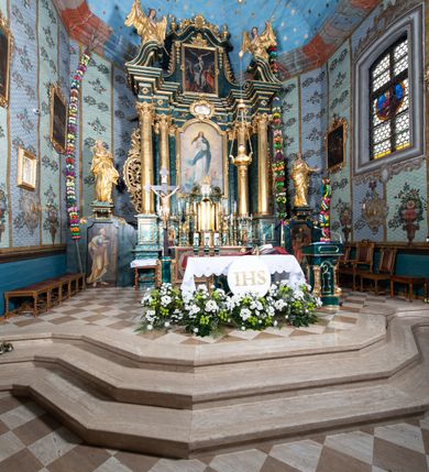 Zdjęcie nr 24: Nastawa ołtarzowa architektoniczna, jednokondygnacyjna ze zwieńczeniem, jednoosiowa z bramkami. Ołtarz prostopadłościenny, murowany, w drewnianej obudowie, z drewnianą mensą. Antepedium ujęte profilowaną ramą; w polu malowana płycina w formie leżącego prostokąta o zaokrąglonych narożach, wypełniona gałązkami różanymi, z akantowo-regencyjnym kartuszem. W narożach antepedium malowane ptaki siedzące na gałązkach. W polu kartusza ukazana scena męczeństwa św. Szymona i św. Judy Tadeusza, na tle pejzażu. Tabernakulum metalowe, prostopadłościenne, flankowane pilastrami w formie spływów wolutowych zdobionych gałązkami róży, zamknięte od góry profilowanym gzymsem. Drzwiczki w kształcie stojącego prostokąta zamkniętego łukiem odcinkowym nadwieszonym; w polu przedstawienie kielicha z hostią. Tabernakulum wprawione w wysoki cokół, na którym stoi tron wystawienia w formie obrotowej niszy, o wypukłej ściance frontowej i ustawionymi pod kątem ściankami bocznymi. Nisza flankowana parą kolumienek i spływów wolutowych dźwigających belkowanie oraz fragmenty przerwanego, półkolistego przyczółka. Na belkowaniu szczyt z rocaillem, z napisem w polu: „ECCE / TABERNACULUM / DEI”. Nastawa ustawiona na dwustrefowym cokole, z wyodrębnionymi czterema prostopadłościanami, w górnej części zdobionym płycinami. Retabulum ujęte parami pilastrów i filarów o kanelowanych trzonach oraz stojącymi przed nimi w układzie schodkowym kolumnami o kapitelach kompozytowych. Podpory dźwigają pełne belkowanie, wyłamane na ich osi, z przerwanym architrawem nad polem środkowym. Na belkowaniu fragmenty falistego, przerwanego przyczółka z figurami aniołów z arma Christi. W polu środkowym wnęka w formie stojącego prostokąta zamkniętego łukiem odcinkowym nadwieszonym, ujęta profilowaną ramą, z obrazem Najświętszej Marii Panny Niepokalanie Poczętej. Nad nią, w polu belkowania rocaille'owy kartusz z napisem „HI / SUNT VIRI / MISERICORDIAE / [...]ccdis 44”. Zwieńczenie w formie zbliżonej do stojącego prostokąta, ujętego pilastrami przechodzącymi w spływy wolutowe, zamkniętego dwoma fragmentami wolutowego gzymsu. Całość zakończona szczytem utworzonym z muszli i zwisów kwiatowych, flankowanym przez dwa wazony. Zwieńczenie ujęte liśćmi palmowymi. W polu obraz z grupą Ukrzyżowania w formie stojącego prostokąta, w profilowanej ramie, dekorowanej rocaille'm. Nastawa flankowana bramkami zwieńczonymi konsolami, na których stoją figury Marii i św. Jana Ewangelisty. Przejścia w formie stojącego prostokąta o wklęsłych górnych narożach, z drzwiczkami z malowanymi przedstawieniami św. Piotra i św. Pawła. Struktura polichromowana na sposób imitujący marmoryzację w kolorze zielono-niebieskim, z laserunkiem, kolumny, ornamentyka i profile złocone, detal srebrzony.