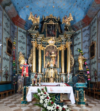 Zdjęcie nr 46: Nastawa ołtarzowa architektoniczna, jednokondygnacyjna ze zwieńczeniem, jednoosiowa z bramkami. Ołtarz prostopadłościenny, murowany, w drewnianej obudowie, z drewnianą mensą. Antepedium ujęte profilowaną ramą; w polu malowana płycina w formie leżącego prostokąta o zaokrąglonych narożach, wypełniona gałązkami różanymi, z akantowo-regencyjnym kartuszem. W narożach antepedium malowane ptaki siedzące na gałązkach. W polu kartusza ukazana scena męczeństwa św. Szymona i św. Judy Tadeusza, na tle pejzażu. Tabernakulum metalowe, prostopadłościenne, flankowane pilastrami w formie spływów wolutowych zdobionych gałązkami róży, zamknięte od góry profilowanym gzymsem. Drzwiczki w kształcie stojącego prostokąta zamkniętego łukiem odcinkowym nadwieszonym; w polu przedstawienie kielicha z hostią. Tabernakulum wprawione w wysoki cokół, na którym stoi tron wystawienia w formie obrotowej niszy, o wypukłej ściance frontowej i ustawionymi pod kątem ściankami bocznymi. Nisza flankowana parą kolumienek i spływów wolutowych dźwigających belkowanie oraz fragmenty przerwanego, półkolistego przyczółka. Na belkowaniu szczyt z rocaillem, z napisem w polu: „ECCE / TABERNACULUM / DEI”. Nastawa ustawiona na dwustrefowym cokole, z wyodrębnionymi czterema prostopadłościanami, w górnej części zdobionym płycinami. Retabulum ujęte parami pilastrów i filarów o kanelowanych trzonach oraz stojącymi przed nimi w układzie schodkowym kolumnami o kapitelach kompozytowych. Podpory dźwigają pełne belkowanie, wyłamane na ich osi, z przerwanym architrawem nad polem środkowym. Na belkowaniu fragmenty falistego, przerwanego przyczółka z figurami aniołów z arma Christi. W polu środkowym wnęka w formie stojącego prostokąta zamkniętego łukiem odcinkowym nadwieszonym, ujęta profilowaną ramą, z obrazem Najświętszej Marii Panny Niepokalanie Poczętej. Nad nią, w polu belkowania rocaille'owy kartusz z napisem „HI / SUNT VIRI / MISERICORDIAE / [...]ccdis 44”. Zwieńczenie w formie zbliżonej do stojącego prostokąta, ujętego pilastrami przechodzącymi w spływy wolutowe, zamkniętego dwoma fragmentami wolutowego gzymsu. Całość zakończona szczytem utworzonym z muszli i zwisów kwiatowych, flankowanym przez dwa wazony. Zwieńczenie ujęte liśćmi palmowymi. W polu obraz z grupą Ukrzyżowania w formie stojącego prostokąta, w profilowanej ramie, dekorowanej rocaille'm. Nastawa flankowana bramkami zwieńczonymi konsolami, na których stoją figury Marii i św. Jana Ewangelisty. Przejścia w formie stojącego prostokąta o wklęsłych górnych narożach, z drzwiczkami z malowanymi przedstawieniami św. Piotra i św. Pawła. Struktura polichromowana na sposób imitujący marmoryzację w kolorze zielono-niebieskim, z laserunkiem, kolumny, ornamentyka i profile złocone, detal srebrzony.