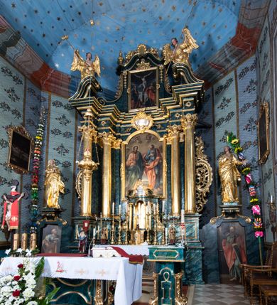 Zdjęcie nr 57: Nastawa ołtarzowa architektoniczna, jednokondygnacyjna ze zwieńczeniem, jednoosiowa z bramkami. Ołtarz prostopadłościenny, murowany, w drewnianej obudowie, z drewnianą mensą. Antepedium ujęte profilowaną ramą; w polu malowana płycina w formie leżącego prostokąta o zaokrąglonych narożach, wypełniona gałązkami różanymi, z akantowo-regencyjnym kartuszem. W narożach antepedium malowane ptaki siedzące na gałązkach. W polu kartusza ukazana scena męczeństwa św. Szymona i św. Judy Tadeusza, na tle pejzażu. Tabernakulum metalowe, prostopadłościenne, flankowane pilastrami w formie spływów wolutowych zdobionych gałązkami róży, zamknięte od góry profilowanym gzymsem. Drzwiczki w kształcie stojącego prostokąta zamkniętego łukiem odcinkowym nadwieszonym; w polu przedstawienie kielicha z hostią. Tabernakulum wprawione w wysoki cokół, na którym stoi tron wystawienia w formie obrotowej niszy, o wypukłej ściance frontowej i ustawionymi pod kątem ściankami bocznymi. Nisza flankowana parą kolumienek i spływów wolutowych dźwigających belkowanie oraz fragmenty przerwanego, półkolistego przyczółka. Na belkowaniu szczyt z rocaillem, z napisem w polu: „ECCE / TABERNACULUM / DEI”. Nastawa ustawiona na dwustrefowym cokole, z wyodrębnionymi czterema prostopadłościanami, w górnej części zdobionym płycinami. Retabulum ujęte parami pilastrów i filarów o kanelowanych trzonach oraz stojącymi przed nimi w układzie schodkowym kolumnami o kapitelach kompozytowych. Podpory dźwigają pełne belkowanie, wyłamane na ich osi, z przerwanym architrawem nad polem środkowym. Na belkowaniu fragmenty falistego, przerwanego przyczółka z figurami aniołów z arma Christi. W polu środkowym wnęka w formie stojącego prostokąta zamkniętego łukiem odcinkowym nadwieszonym, ujęta profilowaną ramą, z obrazem Najświętszej Marii Panny Niepokalanie Poczętej. Nad nią, w polu belkowania rocaille'owy kartusz z napisem „HI / SUNT VIRI / MISERICORDIAE / [...]ccdis 44”. Zwieńczenie w formie zbliżonej do stojącego prostokąta, ujętego pilastrami przechodzącymi w spływy wolutowe, zamkniętego dwoma fragmentami wolutowego gzymsu. Całość zakończona szczytem utworzonym z muszli i zwisów kwiatowych, flankowanym przez dwa wazony. Zwieńczenie ujęte liśćmi palmowymi. W polu obraz z grupą Ukrzyżowania w formie stojącego prostokąta, w profilowanej ramie, dekorowanej rocaille'm. Nastawa flankowana bramkami zwieńczonymi konsolami, na których stoją figury Marii i św. Jana Ewangelisty. Przejścia w formie stojącego prostokąta o wklęsłych górnych narożach, z drzwiczkami z malowanymi przedstawieniami św. Piotra i św. Pawła. Struktura polichromowana na sposób imitujący marmoryzację w kolorze zielono-niebieskim, z laserunkiem, kolumny, ornamentyka i profile złocone, detal srebrzony.