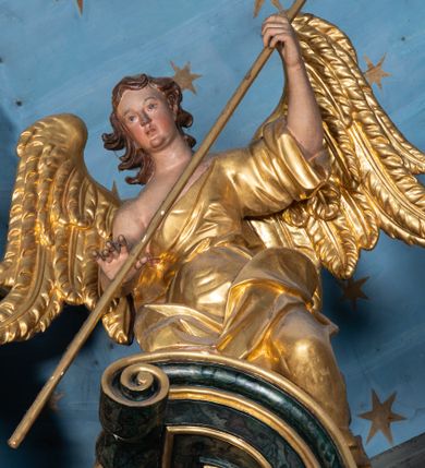 Zdjęcie nr 1: Rzeźby drążone z tyłu, klęczące na fragmentach przerwanego przyczółka, zwrócone do wewnątrz, pochylone. Lewy anioł w uniesionej lewej ręce trzyma laskę zakończoną gąbką, prawą kładzie na piersi. Prawy anioł obiema rękami trzyma włócznię. Twarze mają pociągłe, z wyodrębnionymi brodami, o małych oczach z głęboko rzeźbionymi górnymi powiekami, krótkimi nosami i pełnymi ustami, okolone kręconymi, brązowymi włosami, sięgającymi ramion. Anioły ubrane są w złocone tuniki z jednym rękawem, odsłaniające połowę torsu i drugie ramię, przepasane w talii. Skrzydła mają duże i złożone po bokach. Polichromia ciał naturalistyczna. 

