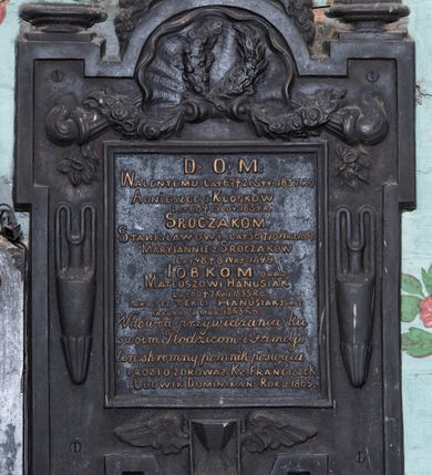 Zdjęcie nr 2: Epitafium w formie tablicy o kształcie stojącego prostokąta ujętej grubą ramą z uszakami w narożach, zamkniętej półkoliście od góry i dołu. W górnej części ramy muszla z podwieszonymi zwisami kwiatowymi, zawiniętymi na palących się pochodniach. Po bokach ramy dwa wąskie wazony, u spodu uskrzydlona klepsydra. Epitafium zwieńczone dekoracją roślinną z krzyżem, na górnych uszakach ustawione dla płaskie wazony, dolne zakończone muszlami. W polu złocony napis „D(EO) O(PTIMO) M(AXIMO) / WALENTEMU LAT 67 † 21 STY(CZNA) 1837. RO[KU] / AGNIESZCE Z KLÓSKÓW / LAT 60 † 15 LUT(EGO) 1834. R(OKU) / SROCZAKOM. / STANISŁAWOWI LAT 58 † 10 WRZ(EŚNIA) 1840 / MARYIANNIE Z SROCZAKÓW / LAT 48 † 8 WRZ(EŚNIA) 1849. / IOBKOM ORAZ / MATEUSZOWI HANUSIAK / LAT 60 † 7 KWI(ETNIA) 1855 RO(KU) / IAKO TEZ TEKLI HANUSIAK ZONIE / IAKUBA ZMAR(ŁEGO) 1863 RO(KU) / W dowód przywiązania ku / swoim Rodzicom i Familiji / ten skromny pomnik poświęca / I PROSI O ZDROWAŚ : KS(IĄDZ) FRANCISZEK / LUDWIK DOMINIKAN ROKU 1865.”