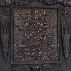 Zdjęcie nr 1: Epitafium w formie tablicy o kształcie stojącego prostokąta ujętej grubą ramą z uszakami w narożach, zamkniętej półkoliście od góry i dołu. W górnej części ramy muszla z podwieszonymi zwisami kwiatowymi, zawiniętymi na palących się pochodniach. Po bokach ramy dwa wąskie wazony, u spodu uskrzydlona klepsydra. Epitafium zwieńczone dekoracją roślinną z krzyżem, na górnych uszakach ustawione dla płaskie wazony, dolne zakończone muszlami. W polu złocony napis „D(EO) O(PTIMO) M(AXIMO) / WALENTEMU LAT 67 † 21 STY(CZNA) 1837. RO[KU] / AGNIESZCE Z KLÓSKÓW / LAT 60 † 15 LUT(EGO) 1834. R(OKU) / SROCZAKOM. / STANISŁAWOWI LAT 58 † 10 WRZ(EŚNIA) 1840 / MARYIANNIE Z SROCZAKÓW / LAT 48 † 8 WRZ(EŚNIA) 1849. / IOBKOM ORAZ / MATEUSZOWI HANUSIAK / LAT 60 † 7 KWI(ETNIA) 1855 RO(KU) / IAKO TEZ TEKLI HANUSIAK ZONIE / IAKUBA ZMAR(ŁEGO) 1863 RO(KU) / W dowód przywiązania ku / swoim Rodzicom i Familiji / ten skromny pomnik poświęca / I PROSI O ZDROWAŚ : KS(IĄDZ) FRANCISZEK / LUDWIK DOMINIKAN ROKU 1865.”