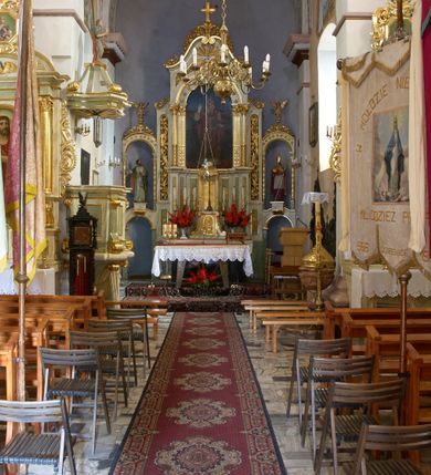 Zdjęcie nr 5: Ołtarz przyścienny, architektoniczny, jednoosiowy z bramkami, jednokondygnacyjny ze zwieńczeniem. Mensa prostopadłościenna, drewniana. Tabernakulum dwukondygnacyjne z tronem wystawienia. Kondygnacja pierwsza ujęta spływami wolutowymi, na drzwiczkach płycina w kształcie stojącego prostokąta zamkniętego łukiem półkolistym z płaskorzeźbionym kielichem z hostią w otoczeniu winorośli. W kondygnacji drugiej tron wystawienia zwieńczony baldachimem wspartym na smukłych kolumienkach z kompozytowymi kapitelami i takich samych pilastrach. Trzony podpór do jednej trzeciej wysokości dekorowane arabeską, powyżej kanelowane. U szczytu baldachimu srebrzony baranek leżący na księdze. Retabulum umieszczone na  wysokim cokole ozdobionym płycinami wypełnionymi dekoracją akantową. Cokół zwieńczony profilowanym gzymsem, na którym ustawione zdwojone podpory: w osiach środkowych złocone pilastry o kanelowanych trzonach dekorowanych w dolnej części arabeską oraz kompozytowych kapitelach; w osiach skrajnych kolumny o analogicznej jak w przypadku pilastrów dekoracji. Pole środkowe ołtarza w kształcie stojącego prostokąta zamkniętego łukiem półkolistym dekorowanym złoconymi kwiatami mieści obraz Matki Boskiej Śnieżnej oraz obraz św. Mikołaja (na zasuwie). Zwieńczenie w formie przyczółka utworzonego z dwóch, przeciwstawnie ustawionych wolut z centralnie umieszczonym złoconym krzyżem oraz ażurową, akantową strukturą; w polu płaskorzeźbiona gołębica Ducha Świętego na tle glorii promienistej. Oś środkowa ujęta dwiema wąskimi płycinami mieszczącymi złocony ornament akantowy. Bramki o formie architektonicznej, jednoosiowe, dwukondygnacyjne ze zwieńczeniem. Kondygnacja pierwsza w formie półkolistej arkady; w zworniku łuku złocona, wolutowa konsolka, na której  ustawiony prostopadłościenny postument z polichromowaną figurą św. Piotra (z lewej) i św. Stanisława (z prawej). Kondygnacja druga ujęta złoconymi korynckimi kolumienkami o skręconych trzonach dźwigającymi łuk półkolisty dekorowany złoconymi, płaskorzeźbionymi kwiatami. W zwieńczeniu pełnoplastyczne, polichromowane figurki puttów ustawione na kulistych konsolkach. Struktura ołtarza polichromowana (w tym marmoryzowana) w dwóch odcieniach jasnej zieleni. Elementy architektoniczne oraz ornamenty złocone.