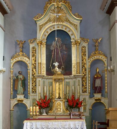 Zdjęcie nr 1: Ołtarz przyścienny, architektoniczny, jednoosiowy z bramkami, jednokondygnacyjny ze zwieńczeniem. Mensa prostopadłościenna, drewniana. Tabernakulum dwukondygnacyjne z tronem wystawienia. Kondygnacja pierwsza ujęta spływami wolutowymi, na drzwiczkach płycina w kształcie stojącego prostokąta zamkniętego łukiem półkolistym z płaskorzeźbionym kielichem z hostią w otoczeniu winorośli. W kondygnacji drugiej tron wystawienia zwieńczony baldachimem wspartym na smukłych kolumienkach z kompozytowymi kapitelami i takich samych pilastrach. Trzony podpór do jednej trzeciej wysokości dekorowane arabeską, powyżej kanelowane. U szczytu baldachimu srebrzony baranek leżący na księdze. Retabulum umieszczone na  wysokim cokole ozdobionym płycinami wypełnionymi dekoracją akantową. Cokół zwieńczony profilowanym gzymsem, na którym ustawione zdwojone podpory: w osiach środkowych złocone pilastry o kanelowanych trzonach dekorowanych w dolnej części arabeską oraz kompozytowych kapitelach; w osiach skrajnych kolumny o analogicznej jak w przypadku pilastrów dekoracji. Pole środkowe ołtarza w kształcie stojącego prostokąta zamkniętego łukiem półkolistym dekorowanym złoconymi kwiatami mieści obraz Matki Boskiej Śnieżnej oraz obraz św. Mikołaja (na zasuwie). Zwieńczenie w formie przyczółka utworzonego z dwóch, przeciwstawnie ustawionych wolut z centralnie umieszczonym złoconym krzyżem oraz ażurową, akantową strukturą; w polu płaskorzeźbiona gołębica Ducha Świętego na tle glorii promienistej. Oś środkowa ujęta dwiema wąskimi płycinami mieszczącymi złocony ornament akantowy. Bramki o formie architektonicznej, jednoosiowe, dwukondygnacyjne ze zwieńczeniem. Kondygnacja pierwsza w formie półkolistej arkady; w zworniku łuku złocona, wolutowa konsolka, na której  ustawiony prostopadłościenny postument z polichromowaną figurą św. Piotra (z lewej) i św. Stanisława (z prawej). Kondygnacja druga ujęta złoconymi korynckimi kolumienkami o skręconych trzonach dźwigającymi łuk półkolisty dekorowany złoconymi, płaskorzeźbionymi kwiatami. W zwieńczeniu pełnoplastyczne, polichromowane figurki puttów ustawione na kulistych konsolkach. Struktura ołtarza polichromowana (w tym marmoryzowana) w dwóch odcieniach jasnej zieleni. Elementy architektoniczne oraz ornamenty złocone.