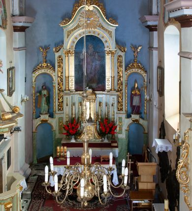 Zdjęcie nr 3: Ołtarz przyścienny, architektoniczny, jednoosiowy z bramkami, jednokondygnacyjny ze zwieńczeniem. Mensa prostopadłościenna, drewniana. Tabernakulum dwukondygnacyjne z tronem wystawienia. Kondygnacja pierwsza ujęta spływami wolutowymi, na drzwiczkach płycina w kształcie stojącego prostokąta zamkniętego łukiem półkolistym z płaskorzeźbionym kielichem z hostią w otoczeniu winorośli. W kondygnacji drugiej tron wystawienia zwieńczony baldachimem wspartym na smukłych kolumienkach z kompozytowymi kapitelami i takich samych pilastrach. Trzony podpór do jednej trzeciej wysokości dekorowane arabeską, powyżej kanelowane. U szczytu baldachimu srebrzony baranek leżący na księdze. Retabulum umieszczone na  wysokim cokole ozdobionym płycinami wypełnionymi dekoracją akantową. Cokół zwieńczony profilowanym gzymsem, na którym ustawione zdwojone podpory: w osiach środkowych złocone pilastry o kanelowanych trzonach dekorowanych w dolnej części arabeską oraz kompozytowych kapitelach; w osiach skrajnych kolumny o analogicznej jak w przypadku pilastrów dekoracji. Pole środkowe ołtarza w kształcie stojącego prostokąta zamkniętego łukiem półkolistym dekorowanym złoconymi kwiatami mieści obraz Matki Boskiej Śnieżnej oraz obraz św. Mikołaja (na zasuwie). Zwieńczenie w formie przyczółka utworzonego z dwóch, przeciwstawnie ustawionych wolut z centralnie umieszczonym złoconym krzyżem oraz ażurową, akantową strukturą; w polu płaskorzeźbiona gołębica Ducha Świętego na tle glorii promienistej. Oś środkowa ujęta dwiema wąskimi płycinami mieszczącymi złocony ornament akantowy. Bramki o formie architektonicznej, jednoosiowe, dwukondygnacyjne ze zwieńczeniem. Kondygnacja pierwsza w formie półkolistej arkady; w zworniku łuku złocona, wolutowa konsolka, na której  ustawiony prostopadłościenny postument z polichromowaną figurą św. Piotra (z lewej) i św. Stanisława (z prawej). Kondygnacja druga ujęta złoconymi korynckimi kolumienkami o skręconych trzonach dźwigającymi łuk półkolisty dekorowany złoconymi, płaskorzeźbionymi kwiatami. W zwieńczeniu pełnoplastyczne, polichromowane figurki puttów ustawione na kulistych konsolkach. Struktura ołtarza polichromowana (w tym marmoryzowana) w dwóch odcieniach jasnej zieleni. Elementy architektoniczne oraz ornamenty złocone.