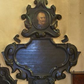 Zdjęcie nr 1: Epitafium z fantazyjnie wyciętą płyciną wpisaną w leżący prostokąt o bokach w kształcie półkolistych, nadwieszonych łuków na wklęsłych uskokach, ujętą uproszczonymi wolutami z chrząstkami. Pod dolną krawędzią kartusz z tarczą z godłami herbów Rola, Doliwa, Łodzia, Topór. Epitafium wieńczy owalne pole z portretem zmarłego otoczony ornamentem kartuszowo-zawijanym i zwieńczony krzyżem wspartym na trzech kulach. Zmarły przedstawiony został w popiersiu, w trzech czwartych. Jego twarz jest pociągła, oczy szeroko otwarte, zwrócone w prawo, nos długi, pod nim wąs, głowa z podgolonymi bokami. W polu inskrypcja „D(EO) O(PTIMO) M(AXIMO) / SIS∙TE GRADVM VIATOR / MAESTA CERNES / HVNC TVMVLV(S) MAGNI VIRI SARCOPHAGVM DOLORVM CVMVLVM ESSE. / NEMPE / MAGNI(ICVS) MATHIAS ALEXANDER A TARNOW TARNOWSKI G(E)N(ERO)SI PAVLICV(M) GRISELI DE ZIELENCKA PROCREAT(VS) / FILIVS / VENATOR PALATINATVS LANCICIENSIS, AC DVCATVS SEVERIAE CAPITANEVS / VIR / CVLTV IN DEV(M) ET DEIPARA(M) HONORE TVM SANCTOS DEI RELIGIONE ERGA RE(I)PVB(LIC)AM AMORE, LIBERTATEM ZELO, / DOMVM SVAM STVDIO, AC MERITIS AMICOS VICINOSQVE OFFICIO / INSIGNIS, / ATQ(VE) MORVM INTEGRITATE LITERARVM SCIENTIA RERVM POLITICARVM PRVDENTIA CONSILIO MATVRO / AMICORVM AMORE, FVNCTIONVM EXPEDITARVM AD COMITIA ET TRIBVNAL DEXTERITATE / CONSPICTVS / FLOS ROSARVM ROSEVS IPSO VERIS INITIO MORTE DECERPTVS / CADIT / OBIVIT IN ARCE SEVERI(AE) A(NNO) CHR(ISTO) MDC. XCVIII. CALEN(DIS) APR(ILIS)AETAT(IS) SVAE LVII / CVI / MAGNIF(ICVS) MICHAEL STANISLA(VS), VENATOR PAL(A)T(INATUS), LANCICIEN(SI) DVCAT(US), SEVER(IENSIS) CAPIT(ANEUS) / ET PERIL(LUSTRIS) AC R(EVERE)ND(V)S ADAM, PAVL(US), PRAEP(OSI)T(US), SEVERIEN(SIS) LVGENTES FILII / DESIDERATISSIMO PARENTI / HVNC LAPIDEM POSVERE. / LECTOR / FIDELIB(VS) DEFVN(CTIS) REQVIE(M) P[RE]CARE SE(MPI)T(E)RNA(M)”.
