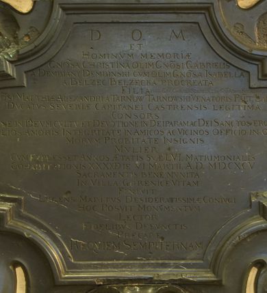 Zdjęcie nr 3: Epitafium z fantazyjnie wyciętą płyciną wpisaną w leżący prostokąt o bokach w kształcie półkolistych, nadwieszonych łukach na wklęsłych uskokach, ujętą uproszczonymi wolutami z chrząstkami. Pod dolną krawędzią kartusz z tarczą z godłami herbów Rawicz, Jastrzębiec, Ramułt, Korybut. Epitafium wieńczy owalne pole z portretem zmarłej otoczone ornamentem kartuszowo-zawijanym i zwieńczone krzyżem wspartym na trzech kulach. Kobieta została przedstawiona w popiersiu, w trzech czwartych, w koronkowym welonie oraz ze sznurem pereł na szyi. Twarz z migdałowatymi oczami zwróconymi w lewo, z długim nosem i wąskimi, szerokimi ustami. W polu inskrypcja „D(EO) O(PTIMO) M(AXIMO) / ET / HOMINVM MEMORIAE / G(E)N(ER)OSA CHRISTINA OLIM G(E)N(E)OSI GABRIELIS / A DEMBIANY DEMBINSKI CVM OLIM G(E)N(ER)OSA ISABELLA / A BELZEC BELZECKA PROCREATA / FILIA [obok wykutE wtórnie Primo CAROLI SZEMBEK 2do G(ENERO)SI ADAMI KOCHANSKI ultimo VOTO G(E)N(ER)OSI MATTHIAE ALEXANDRI A TARNOW TARNOWSKI VENATORIS PAL(A)TINI LANCICZE[SIS] / DVCATVS SEVERIAE CAPITANEI CASTRENSIS LEGITIMA / CONSORS / RELIGIONE IN DEVM CVLTV ET DEVOTIONE IN DEI PARAM AC DEI SANCTOS ERGA MARITVM / AC FILIOS AMORIS INTEGRITATE IN AMICOS AC VICINOS OFFICIO IN OMNES / MORVM PROBITATE INSIGNIS / MVLIER / CVM EXPLESSET ANNOS AETATES SVAE LVI MATRIMONIALIS / COHABITATIONIS XXXX DIE VI MARTII. A(NNO) D(OMINI) M.D.CXCV / SACRAMENTIS BENE MVNITA / IN VILLA GORENICE VITAM / FINIVIT. / LVGENS MARITIVS DESIDERATISSIMAE CONIVGI / HOC POSVIT MONVMENTVM / LECTOR / FIDELIBVS DEFVNCTIS / PRECARE / REQVIEM SEMPITERNAM.”