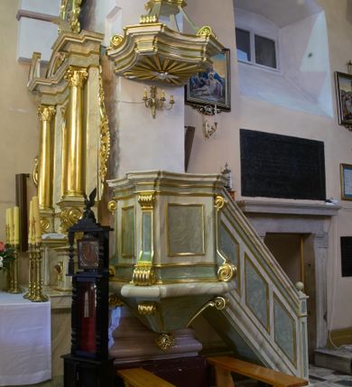 Zdjęcie nr 1: Ambona przyścienna, drewniana, polichromowana i złocona, z baldachimem, dostępna schodkami od strony prezbiterium. Kosz ambony na rzucie czworoboku o ściętych narożach oraz wklęsłych bokach ustawiony na profilowanym cokole, ujęty w narożach wolutowymi pilastrami dźwigającymi bogato profilowane, pełne belkowanie z wydatnym gzymsem. Pola kosza wklęsłe, dekorowane prostokątnymi płycinami. Całość ujęta od dołu czterema wolutami; pod spodem podwieszone pełnoplastyczne, złocone winne grono. Baldachim na rzucie czworoboku o ściętych narożach i wklęsłych bokach; bogato profilowany. Zwieńczony pełnoplastyczną, polichromowaną figurą św. Jana Ewangelisty trzymającego kielich ustawioną na ażurowej konsoli wspartej na wolutach. Na podniebiu płaskorzeźbione, złocone i srebrzone przedstawienie gołębicy Ducha Świętego. Ambona polichromowana (w tym marmoryzowana) w dwóch odcieniach jasnej, pastelowej zieleni. Detale elementów architektonicznych złocone. Figura św. Jana w pełni polichromowana.