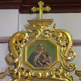 Zdjęcie nr 1: Płaskorzeźba w kształcie ośmioboku ujęta profilowaną, złoconą ramką oraz ażurowym obramieniem utworzonym z przeciwstawnie ułożonych wolut wzbogaconych ornamentem małżowinowo-chrząstkowym. W zwieńczeniu złocony krzyż o trójlistnie zakończonych ramionach ustawiony na niewielkim postumencie wspartym na strukturze z ornamentu małżowinowo-chrząstkowego. W centralnym polu płaskorzeźbione przedstawienie św. Anny w towarzystwie młodzieńczej Marii. Święta ukazana w popiersiu, frontalnie, z głową uniesioną nieznacznie ku górze. Anna została przedstawiona jako dojrzała kobieta ubrana w białą szatę, obszerny, ciemnogranatowy płaszcz ze złotą podszewką oraz żółtą chustę zarzuconą na głowę. Swoją prawą dłoń przyciska do piersi, lewą obejmuje przedstawioną w jasnoróżowej szacie Marię, która czyta z otwartej księgi. Tło jednolicie jasnozielone, postaci polichromowane; partie ornamentu oraz detale szat złocone.

