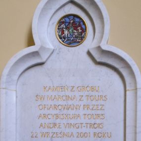 Zdjęcie nr 1: Kamienna tablica pamiątkowa w kształcie stojącego prostokąta  zamkniętego ostrym łukiem trójlistnym  w profilowanej ramie. W górnej części medalion z emaliowanym przedstawieniem  św. Marcina na koniu dzielącego się płaszczem z żebrakiem. W części centralnej złocona inskrypcja „KAMIEŃ Z GROBU / ŚW[IĘTEGO] MARCINA Z TOURS / OFIAROWANY PRZEZ / ARCYBISKUPA TOURS / ANDRE VINGT-TROIS / 22 WRZEŚNIA 2001 ROKU / WMUROWANY PRZEZ / J(EGO) EM(INENCJĘ) KS(IĘDZA) KARDYNAŁA / FRANCISZKA MACHARSKIEGO / 11 LISTOPADA 2002 ROKU”. Poniżej inskrypcji mała kwadratowa, złocona, przeszklona nisza zawierająca kamień z grobu św. Marcina z Tours.