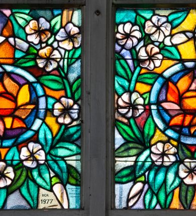 Zdjęcie nr 2: Witraż w zachodnim przęśle nawy, w oknie południowym. Kompozycja w kształcie stojącego prostokąta zamkniętego łukiem ostrym, przedzielona pionową laską na dwie części, u góry z maswerkiem o motywie czteroliścia. Witraż przedstawia scenę wskrzeszenia Piotrowina przez świętego Stanisława Szczepanowskiego. W prawej części św. Stanisław w stroju biskupim, w lewej powstający z grobu Piotrowin. Powyżej banderola z napisem: ŚWIĘTY STANISŁAW, ozdobiona stylizowanymi kwiatami. W górnej części dwa ustawione antytetycznie anioły trzymające na rękach mandorle z atrybutami: mieczem i palmą. W polu czteroliścia herb miasta Kraków. W dolnej części medalion z rozchylonym kwiatem o rozchylonych płatkach otoczony stylizowaną wicią roślinną z białymi kwiatami. Na drugim planie pejzaż z średniowiecznym miastem w tle. Postacie uproszczone, zgeometryzowane, modelunek linearny. Kolory kontrastowe, przewaga zieleni. W prawym dolnym narożu sygnatury: KRAKOWSKI ZAKŁAD WITRAŻY KRASIŃSKIEGO NR. 23, oraz: ROK 1977 / PROJEKTOWAŁ  ART. MAL. BOLESŁAW SZPRECHT.