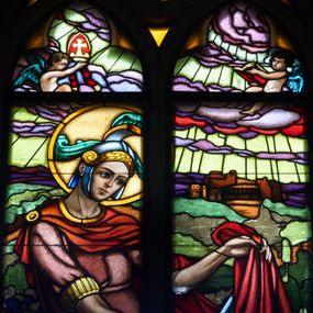 Zdjęcie nr 1: Witraż w prezbiterium w oknie północnym, w kształcie stojącego prostokąta zamkniętego łukiem ostrym. Kompozycja podzielona pionową laską na dwie części, u góry maswerk o motywie czteroliścia. Brak kwater nr 4, 5, 7 i 9 (od góry).  W centrum przedstawienie św. Marcina z Tours jadącego na koniu i oddającego część swojego płaszcza biedakowi. Święty ubrany w zbroję rzymską. W tle pejzaż z elementami architektury. Ponad głową postaci putto trzymające w dłoniach infułę biskupią oraz drugie z księgą. W polu czteroliścia anioł z trąbą. Całość stylizowana na gobelin z dekoracyjnymi chwostami u dołu. W 8 kwaterze napis: PIAE MEMORIAE PARENTUM LADISLAI ET MARIAE / FUNDAVIT A.D. 1938. (napis niekompletny, dalsza część znajdowała się w kwaterze nr 9).