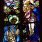 Zdjęcie nr 1: Witraż w prezbiterium w oknie południowym, kształcie stojącego prostokąta zamkniętego łukiem ostrym. Kompozycja podzielona w pionową laską na dwie części, u góry z maswerkiem o motywie czteroliścia. W centrum przestawienie stojącej Marii w białej szacie i niebieskim płaszczu, z koroną na głowie, trzymającej na ramionach Chrystusa, który przekazuje różaniec klęczącemu po lewej stronie św. Dominikowi. Święty ubrany w biały habit oraz błękitny płaszcz. U jego stop leży księga oraz płonąca pochodnia. W tle pejzaż oraz bogata dekoracja roślinna. W górnej części, pod maswerkiem hierogram Chrystusa i splecione litery imienia Maria w obramieniach w kształcie mandorli. W polu czteroliścia przedstawienie kielicha z hostią, po bokach z kiścią winogron i kłosem pszenicy. Dolną część kompozycji wypełnia dekoracja roślinna, w którą wplecione są dwa medaliony, po lewej z sercem Chrystusa (płonące serce, ujęte cierniową koroną, zwieńczone krzyżem), po prawej serce Marii (płonące serce oplecione wieńcem z białych róż, przebite mieczem) – oba serca ujęte glorią promienistą.
