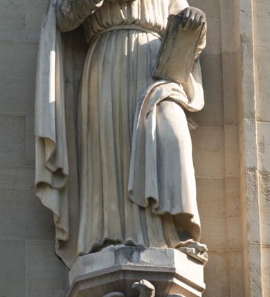 Zdjęcie nr 2: Na konsoli na rzucie ośmioboku, wmurowanej w fasadę, podpieranej przez orła z rozpostartymi skrzydłami, stoi święty ukazany w całej postaci, w kontrapoście, ubrany w długą suknię przepasaną pasem na biodrach i płaszcz, okrywający prawe ramię i dolną część lewej nogi, z prawą ręką uniesioną, z lewą przytrzymującą księgę wspartą na udzie. 

