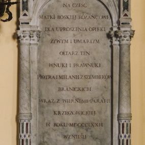 Zdjęcie nr 1: Tablica pamiątkowa w obramieniu w formie neogotyckiej aedikuli ustawionej na konsoli z herbem Branickich. Aedikula jednoosiowa, ujęta kolumnami o kompozytowych kapitelach, ustawionymi na tle pilastrów. Trzony kolumn dołem inkrustowane kolorowym marmurem, wyżej kanelowane. Na kolumnach wsparta trójkątna wimperga zdobiona żabkami i zwieńczona okazałym kwiatonem, flankowana pinaklami. W polu wimpergi dekoracja maswerkowa inkrustowana barwnym marmurem. Na tablicy kuta inskrypcja majuskułowa w języku polskimi: NA CZEŚĆ / MATKI BOSKIEJ / RÓŻAŃCOWEJ / DLA UPROSZENIA OPIEKI / ŻYWYM I UMARŁYM / OŁTARZ TEN / WNUKI I PRAWNUKI / PIOTRA I MELANII / Z SZEMBEKÓW / BRANICKICH / WRAZ Z WIERNEMI PARAFII / KRZESZOWICKIEJ / W ROKU MDCCCLXXII / WZNIEŚLI.