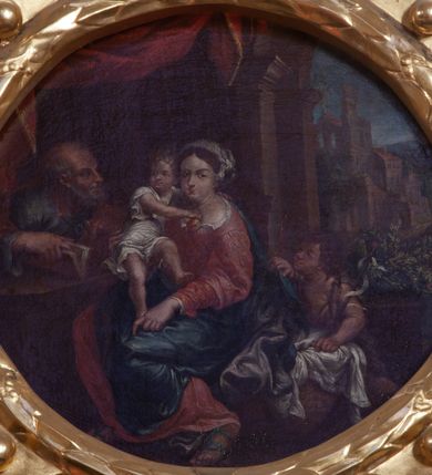 Zdjęcie nr 1: Obraz w kształcie koła (tondo) z przedstawieniem Świętej Rodziny. Pośrodku kompozycji ukazana Matka Boska w pozycji siedzącej, która podtrzymuje stojące na jej kolanach Dzieciątko, lewą ręką ujmując go za nóżkę. Ubrana w szeroką, czerwoną suknię z białym kołnierzem oraz szafirowy płaszcz. Dzieciątko, przewiązane w pasie białą pieluszką, obejmuje Marię za szyję. Po lewej siedzi święty Józef zwrócony ku scenie środkowej. Święty odziany w niebieską suknię i czerwony płaszcz. Po drugiej stronie, obok Marii, aniołek. Ponad postaciami podwieszona czerwona draperia. W tle pejzaż z widokiem Jerozolimy i niebieskie niebo. Obraz ujęty w ramę z wieńca laurowego, otoczonego ażurowym ornamentem o motywie okuciowym, z kwiatonami po bokach i krzyżem w muszli na szczycie.