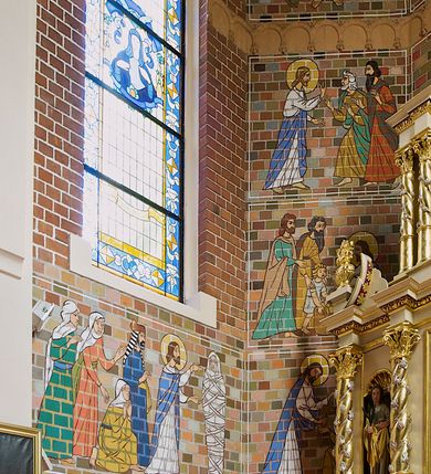 Zdjęcie nr 2: Polichromia, kładziona bezpośrednio na cegłę, pokrywa ściany oraz sklepienie świątyni – na ścianach namalowano sceny figuralne, na sklepieniu dekorację floralną.  Poszczególne sceny na ścianach są ujęte w cienkie białe ramy. Przedstawienia są schematyczne, linearne i obwiedzione konturem. 
Na ścianach prezbiterium od strony północnej przedstawienie Ostatniej Wieczerzy. Chrystus w centrum siedzi na tronie, prawa dłoń uniesiona w geście błogosławieństwa, lewa spoczywa na stole, przed nim kielich i chleb, wokół głowy nimb. Obok Chrystusa symetrycznie rozmieszczeni apostołowie tworzący cztery grupy złożone z trzech apostołów każda. Po przeciwnej stronie scena Zesłania Ducha Świętego. W centrum klęcząca frontalnie Matka Boska, w nimbie wokół głowy, nad nią gołębica Ducha Świętego w glorii. Postać Matki Boskiej i otaczający apostołowie z językami ognia. Powyżej obu przedstawień prostokątne zakończone ostrołukowo płyciny wypełnione w górnej części linearnymi przedstawieniami świętych na białym tle. Na północnej ścianie prezbiterium św. Stanisław Kostka ukazany całopostaciowo, zwrócony w lewą stronę, w habicie przewiązanym sznurem w pasie i w płaszczu. W lewej dłoni trzyma krucyfiks, a w prawej lilię; wokół głowy nimb. U dołu napis: „ŚW. STANISŁAW KOSTKA” . Po przeciwnej stronie bł. Maria Goretti. Postać jest zwrócona w prawą stronę, ubrana w sukienkę i chustę na ramionach, dłonie złożone na piersi, w prawej trzyma palmę męczeństwa. U dołu napis „bł. Maria G[?]oretti” 
Apsyda: 
W najniższym pasie od lewej strony scena Zmartwychwstania. W centrum Chrystus wychodzący z grobu,  ukazany frontalnie, ubrany w czerwony płaszcz, spięty pod szyją, prawa dłoń uniesiona w geście błogosławieństwa, w lewej chorągiew paschalna. Po prawej stronie ukazany siedzący na kamieniu grobowym anioł zwrócony w stroną Chrystusa. Po lewej stojące trzy niewiasty, w dłoniach trzymające naczynia. Wokół głów Chrystusa i anioła nimby. 
Scena przedstawiająca Wieczerzę w Emaus ukazuje trzy postacie siedzące przy stole. Chrystus po lewej stronie, profilem, z prawą dłonią uniesioną w geście błogosławieństwa, w lewej trzymający kulę. Po prawej stronie przedstawieni apostołowie z uniesionymi rękami. Na stole kielich z winem i bochenek chleba. Wszystkie postaci siedzą na krzesłach z wysokimi zapleckami. 
W scenie przedstawiającej wizytę Zbawiciela u Marii i Marty, Chrystus ukazany z prawej strony, z profilu, siedzi na krześle z wysokim zapieckiem, zwrócony w stronę Marii. Prawa dłoń uniesiona w geście oratorskim, lewa spoczywa na kolanie. Maria klęcząca przed Jezusem jest ukazana z profilu. Na drugim planie fragment stołu, na którym stoi biały wazon i bochenek chleba. Z lewej strony postać Marty ukazana frontalnie, z głową skierowaną w stronę Chrystusa, z dłońmi trzymającymi misę. 
W scenie przedstawiającej Złożenie do grobu, w centrum znajduje się Maria trzymająca na kolanach ciało syna, podtrzymywane dodatkowo przez dwie kobiety. Wokół grupy trzy postacie adorujących kobiet. 
 W wyższym rzędzie od lewej strony scena przedstawiająca Wskrzeszenia Łazarza. Z prawej strony stojący Łazarz w śmiertelnym zawoju, po jego lewej stronie Chrystus ukazany niemal profilem, z uniesionymi dłońmi. Za Chrystusem cztery postaci, trzy kobiety i mężczyzna, jedna z kobiet klęczy. 
W kolejnej scenie wyobrażono Jezusa zwróconego w lewo, w stronę św. Piotra, z lewą dłonią wzniesioną do góry i z prawą trzymającą dwa klucze, które przekazuje Piotrowi. Przed nim klęczący, ukazany z profilu św. Piotr, odbierający klucze lewą dłonią. Na drugim planie, za postacią Piotra, stoi dwóch mężczyzn. 
W scenie przedstawiającej przypowieść o talentach, ukazane są cztery kobiety. Z prawej strony kobieta zwrócona w prawą stronę, prawa ręka uniesiona, w dłoni moneta. Z lewej strony, grupa trzech poruszonych kobiet. 
Scena ukazująca Umywanie nóg Chrystusowi przez Marię Magdalenę przedstawia siedzącego Chrystusa zwróconego w prawo, w kierunku klęczącej Marii Magdaleny. Kobieta wyciera jego stopy włosami, obok pojemnik na oleje. Na drugim planie suto zastawiony stół biesiadny, przy nim siedzą trzy postacie umieszczone symetrycznie, w centrum mężczyzna, po jego bokach kobiety. Z lewej strony, stojąca kobieta z misą. 
W trzecim rzędzie od lewej scena przedstawiająca rozmnożenie chleba i ryb. Z prawej strony siedzący Chrystus, ukazany z profilu, zwrócony w prawą stronę. Z dłońmi uniesionymi nad koszem, pełnym ułomków chleba. Przed nim dziecko w prawej dłoni trzymające kosz, w lewej dwie ryby. Za dzieckiem przedstawiono dwóch stojących mężczyzn zwróconych w stronę Chrystusa. 
Kolejna scena przedstawia uzdrowienie chorego. Z prawej strony stojący Chrystus, ukazany z profilu z uniesionymi dłońmi. Z lewej strony grupa trzech osób – kobieta podtrzymywana przez dwóch mężczyzn. 
W następnym rzędzie od lewej scena przedstawiająca Chrystusa z dwoma mężczyznami. Jezus po lewej stronie, ukazany z profilu, zwrócony w lewą stronę, prawa dłoń uniesiona w geście oratorskim. Z prawej strony dwóch kroczących mężczyzn.
następna scena z Barankiem Apokaliptycznym.  W centrum ustawiony jest ołtarz, na którym stoi kielich, nad nim na księdze z siedmioma pieczęciami spoczywa baranek w glorii. Z lewej strony św. Jan Ewangelista, zwrócony w stronę baranka, w lewej dłoni otwarta księga, w prawej pióro. Z prawej strony ustawiony frontalnie św. Jan Chrzciciel, w lewej dłoni trzyma krzyż na długim drzewcu, wokół głów nimby. 
Kolejna scena przedstawia Chrystusa z Samarytanką. Po lewej stronie Jezus siedzący przy studni, ukazany z profilu, zwrócony w lewą stronę, lewa ręka uniesiona, prawa spoczywa na kolanie. Z prawej strony Samarytanka zwrócona w stronę Chrystusa, czerpiąca wodę ze studni. 
W zwieńczeniu prezbiterium od lewej strony św. Andrzej ukazany całopostaciowo, frontalnie, w pomarańczowej tunice, brązowym płaszczu, w lewej ręce ma zamkniętą księgę i pióro gęsie, w prawej podtrzymuje krzyż, wokół głowy nimb. 
W środkowej scenie znajduje się Matka Boska z Dzieciątkiem ukazana całopostaciowo, frontalnie. Maria w białej sukni, niebieskim płaszczu i czerwonych trzewiczkach, na lewym ramieniu trzyma Dzieciątko Jezus ubrane w czerwoną tunikę, prawą dłoń unosi w geście błogosławieństwa, w lewej trzyma jabłko królewskie. Wokół głów nimby.  Po bokach napisy „AVE / MARIA / GRATIA / PLENA”.  
Z prawej strony św. Maria Magdalena ukazana całopostaciowo, frontalnie, w zielonej sukni, pomarańczowym płaszczu, białym welonie na głowie, w prawej dłoni trzyma otwartą księgę, na niej trupia czaszka, na której spoczywa lewa dłoń. Wokół głowy nimb. 
Na ścianie przy łuku tęczowym po stronie północnej przedstawiono  biskupów  św. Stanisława i  św. Wojciecha. Ukazani frontalnie, całopostaciowo, obaj w pełnym stroju biskupim, w lewych dłoniach pastorały, wokół głów nimby. Święty Stanisław z paliuszem na ramionach, prawa dłoń w geście błogosławieństwa, św. Wojciech w rękawiczkach, w prawej dłoni zamknięta księga. U dołu tarcze herbowe, nad nimi napisy „ŚWIETY STANISŁAW BISKUP / ŚWIETY WOJCIECH BISKUP”. 
Na sklepieniach w nawie głównej, prezbiterium i absydzie w polach wydzielanych czerwonym konturem, dekoracja w formie bujniej wici roślino-kwiatowej. W nawie główniej rzadsza. Łuk tęczowy z barwionymi kształtkami – czerwień, pomarańcz, zieleń, granat. Sklepienia naw bocznych – w polach wydzielanych czerwonym konturem, dekoracja w formie symetrycznych dekoracyjnych wstążek, żółto-niebieskich. Sklepienia empor błękitne. 
Ściana chóru – balustrada, w przyłączach wić akantowa, tło groszkowane, na balustradzie przedstawienia dam i królów, na osi godło Polski wyżej napis „966”, postacie ukazane w popiersiu, oddzielone kwiatonami, tło cętkowane. Ściana chórowa z symetrycznym przedstawianiem aniołów w locie, w długich rozwianych szatach, przy pasach falujące wstążki. Anioł po lewej dmący w trąbkę, po prawej oburącz trzyma skrzypce.
