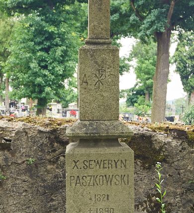 Zdjęcie nr 1: Nagrobek wolnostojący w kształcie dwustrefowego cokołu zwieńczonego krzyżem łacińskim posadowionym na wysokiej, prostopadłościennej podstawie opartej na zwężającym się ku górze cokoliku. Na podstawie krzyża umieszczono chryzmon między greckimi literami A i Ω, a poniżej, na czołowym boku cokołu odkuto inskrypcję „X(IĄDZ) SEWERYN / PASZKOWSKI / *1821 / † 1890”.